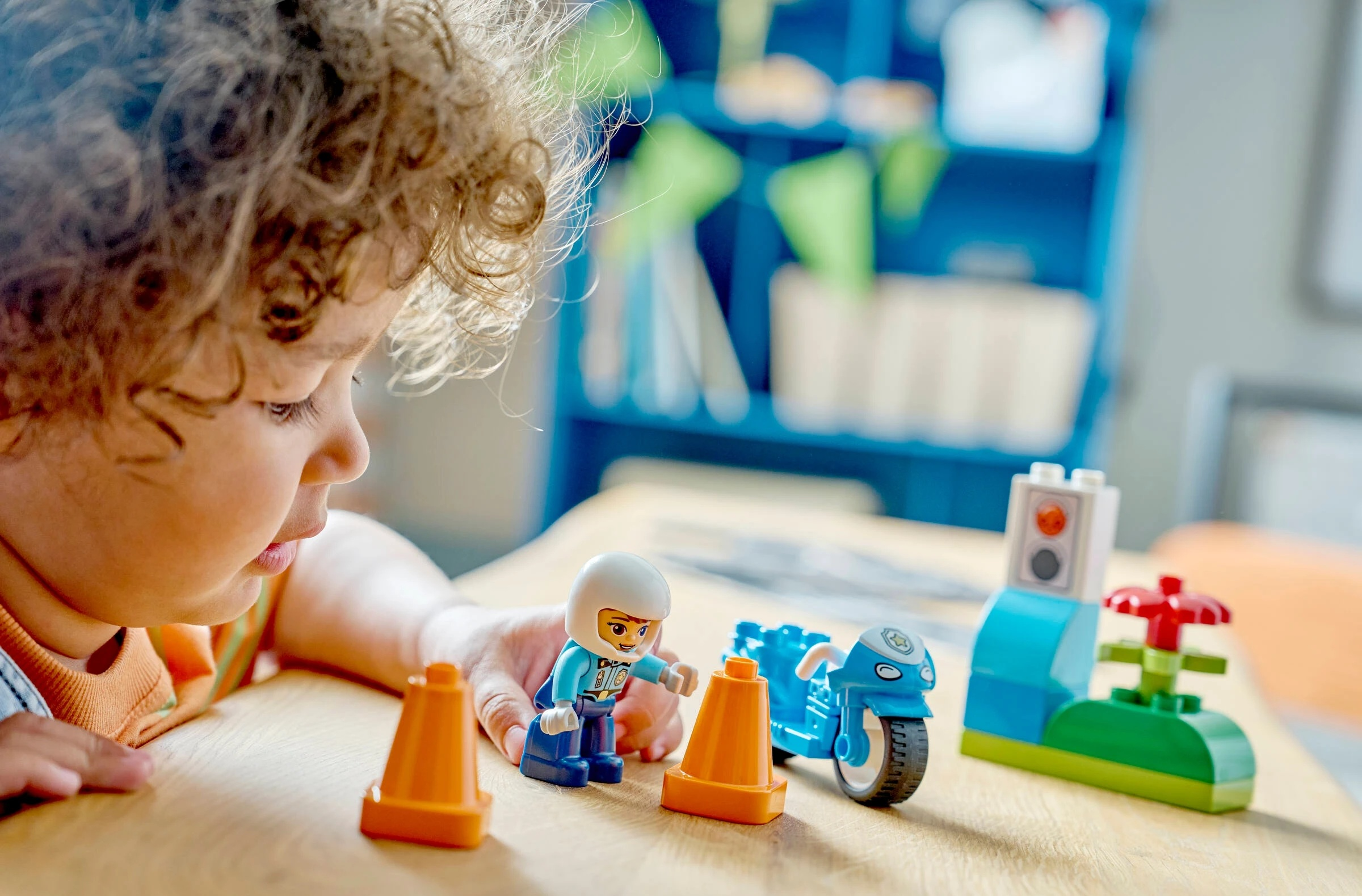 Dziecko bawi się niebieskimi i pomarańczowymi klockami, motocyklem i pachołkami.