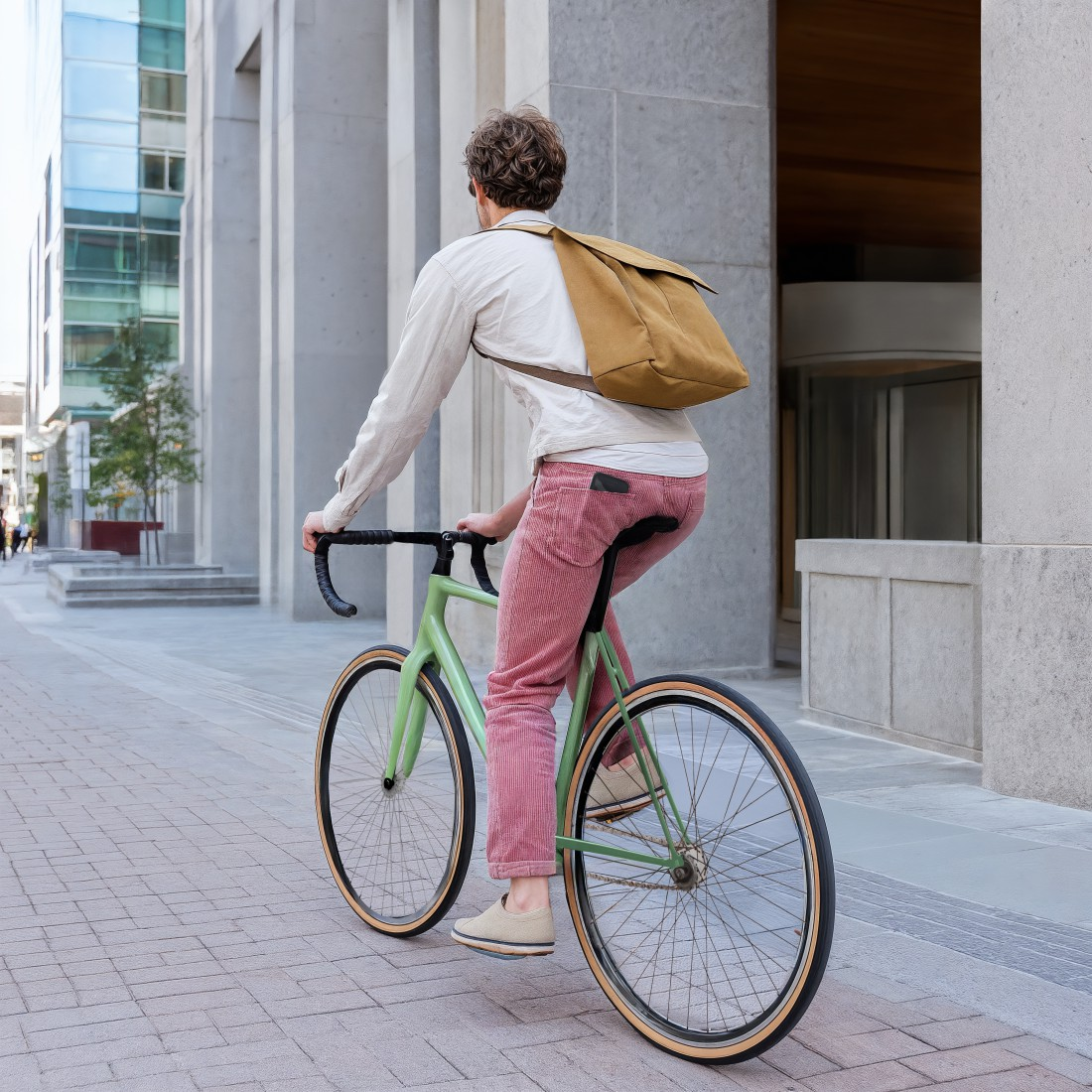 Ein Mann mit braunem Rucksack fährt ein hellgrünes Fahrrad auf einem Gehweg.
