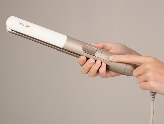 Dłoń trzyma biało-złotą prostownicę, druga naciska przyciski.