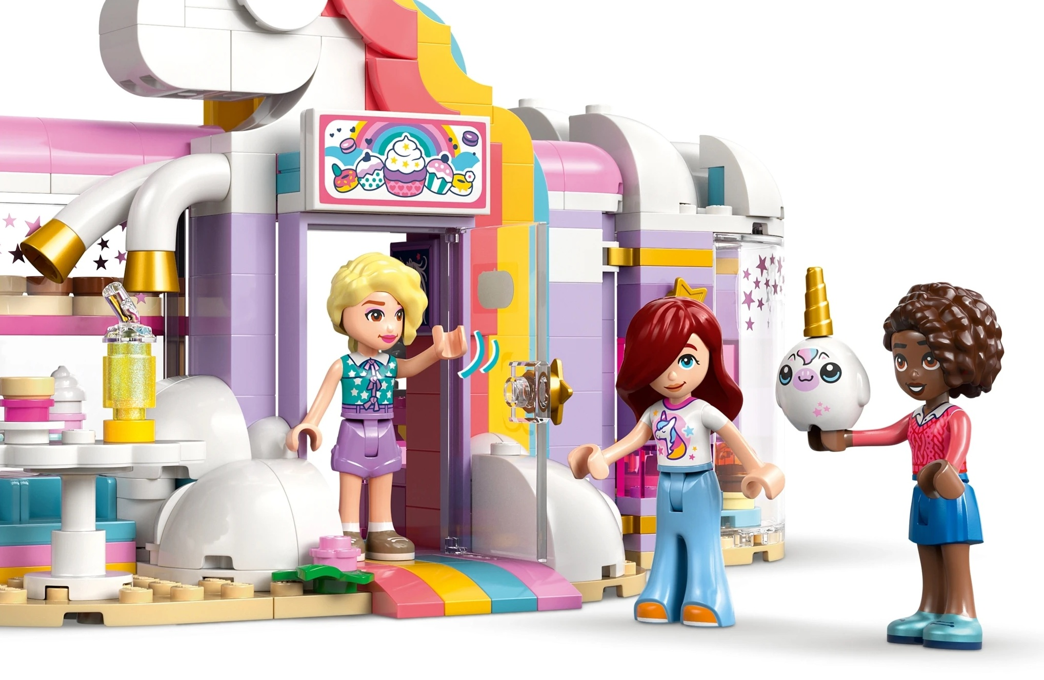 Trzy przyjaciółki Lego przed budynkiem o tematyce jednorożca z babeczkami.