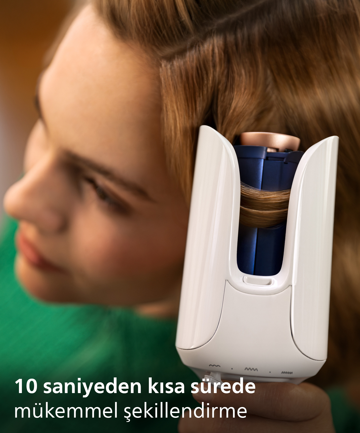 Bir kadın kahverengi saçına otomatik saç maşası kullanıyor.