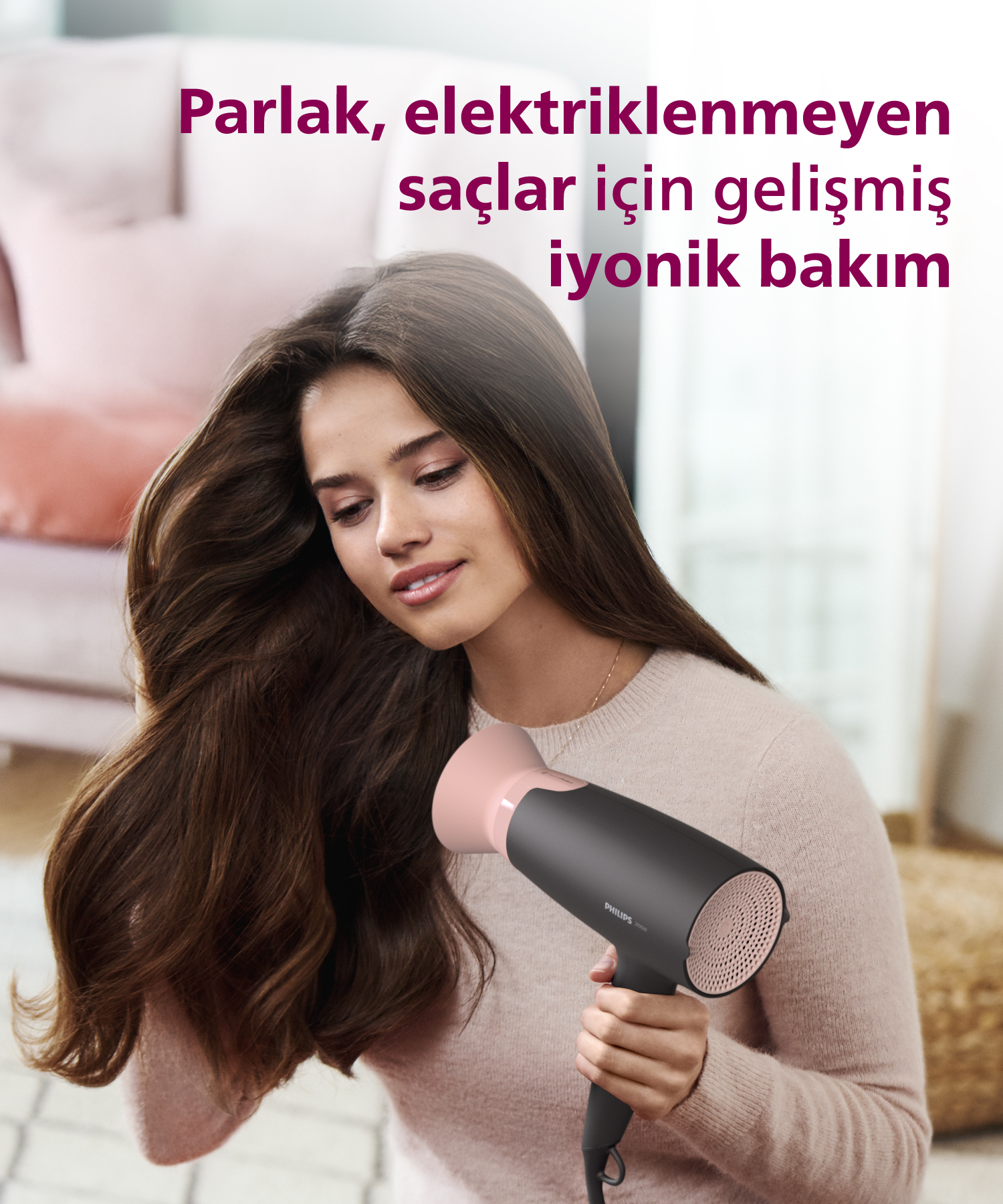 Bir kadın uzun, kahverengi saçlarını siyah ve pembe saç kurutma makinesiyle kurutuyor.