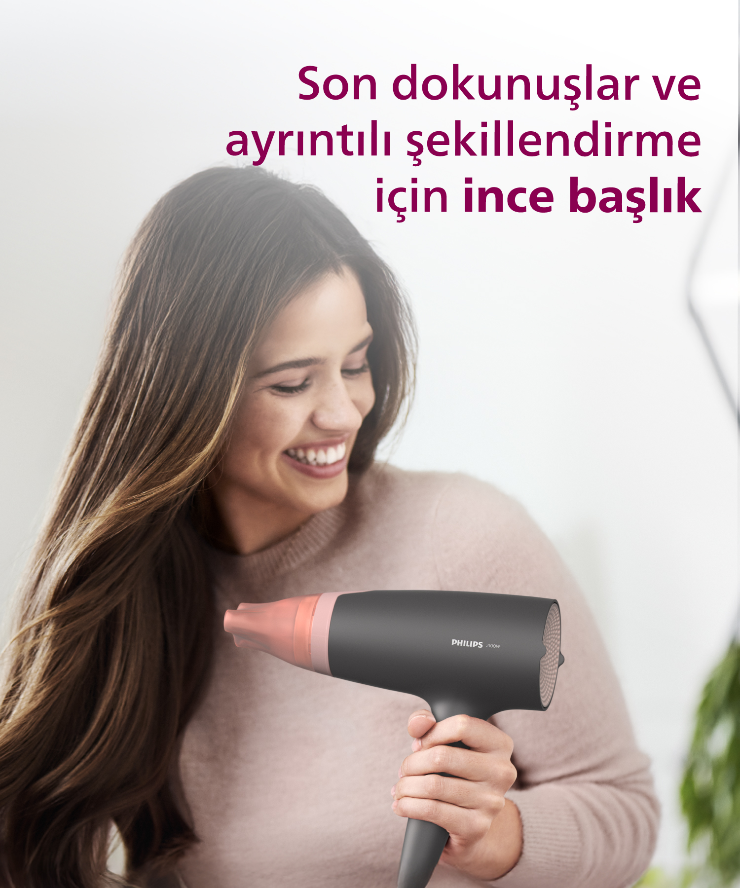 Kadın, pembe başlığı olan koyu renkli bir Philips saç kurutma makinesi tutuyor.