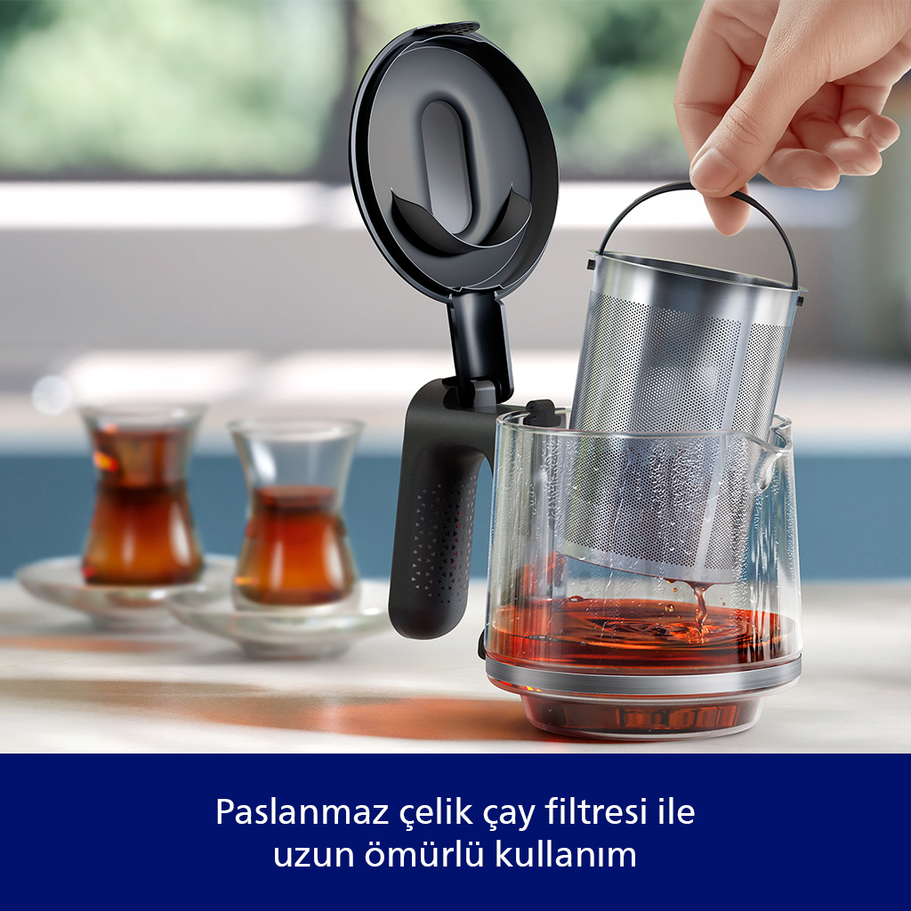Bir el, çay dolu cam demliğe metal çay filtresi yerleştiriyor.