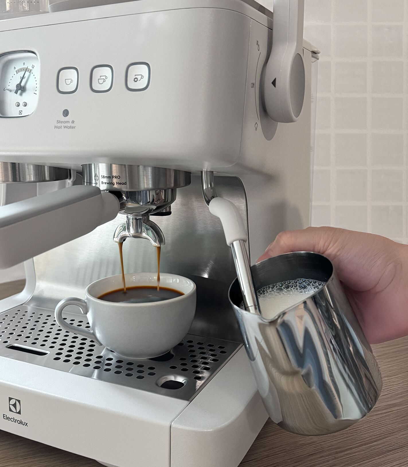 Kahve fincana akarken bir el, süt köpürtücüyü espresso makinesinin üzerinde tutuyor.