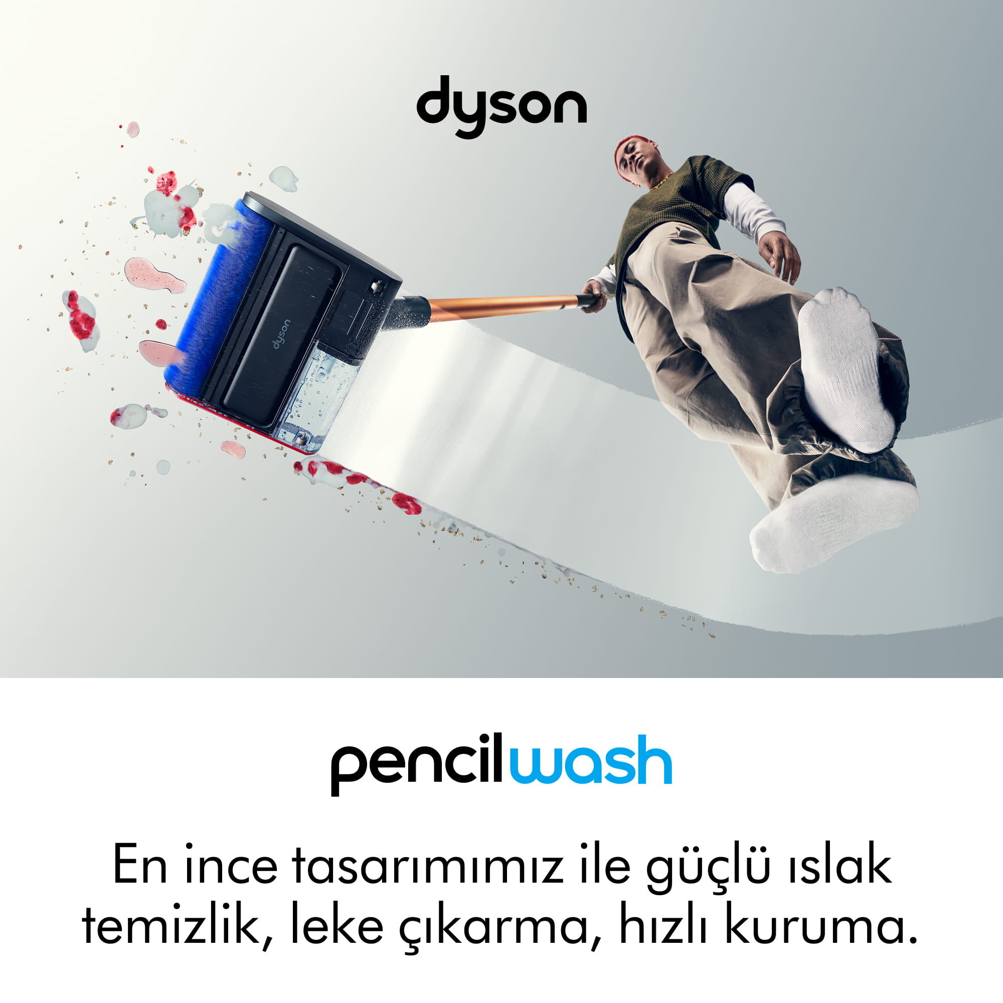 Kızıl saçlı bir adam, kırmızı sıvıyı emen bir Dyson yer temizleyici kullanıyor.