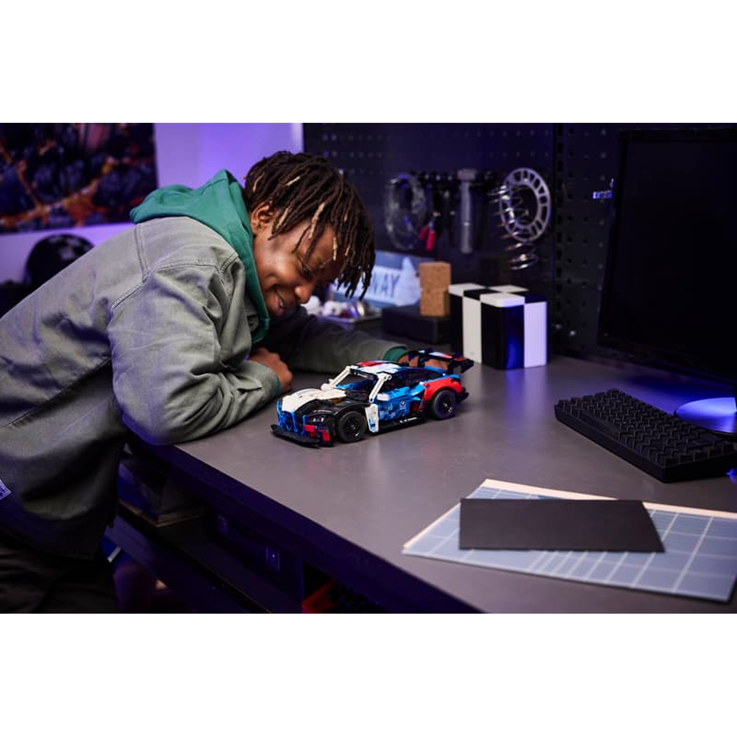 A man leans over a desk looking at a toy car.