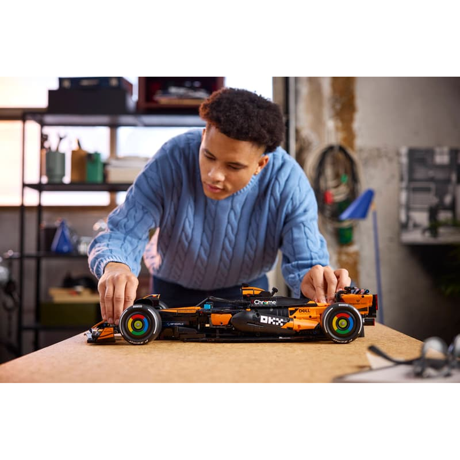 A boy builds an orange and black Formula 1 race car out of LEGO bricks.