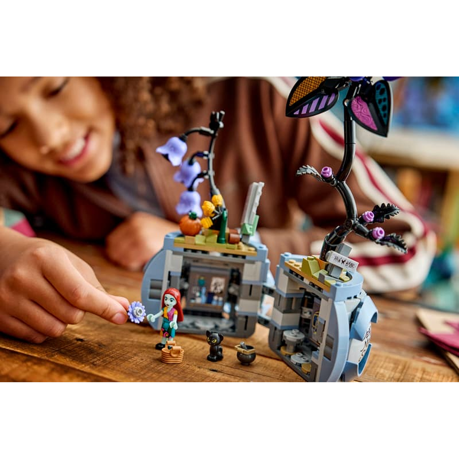 Een kind speelt met Lego-figuren en een blauwe bloemenhuis-speelset op een houten tafel.
