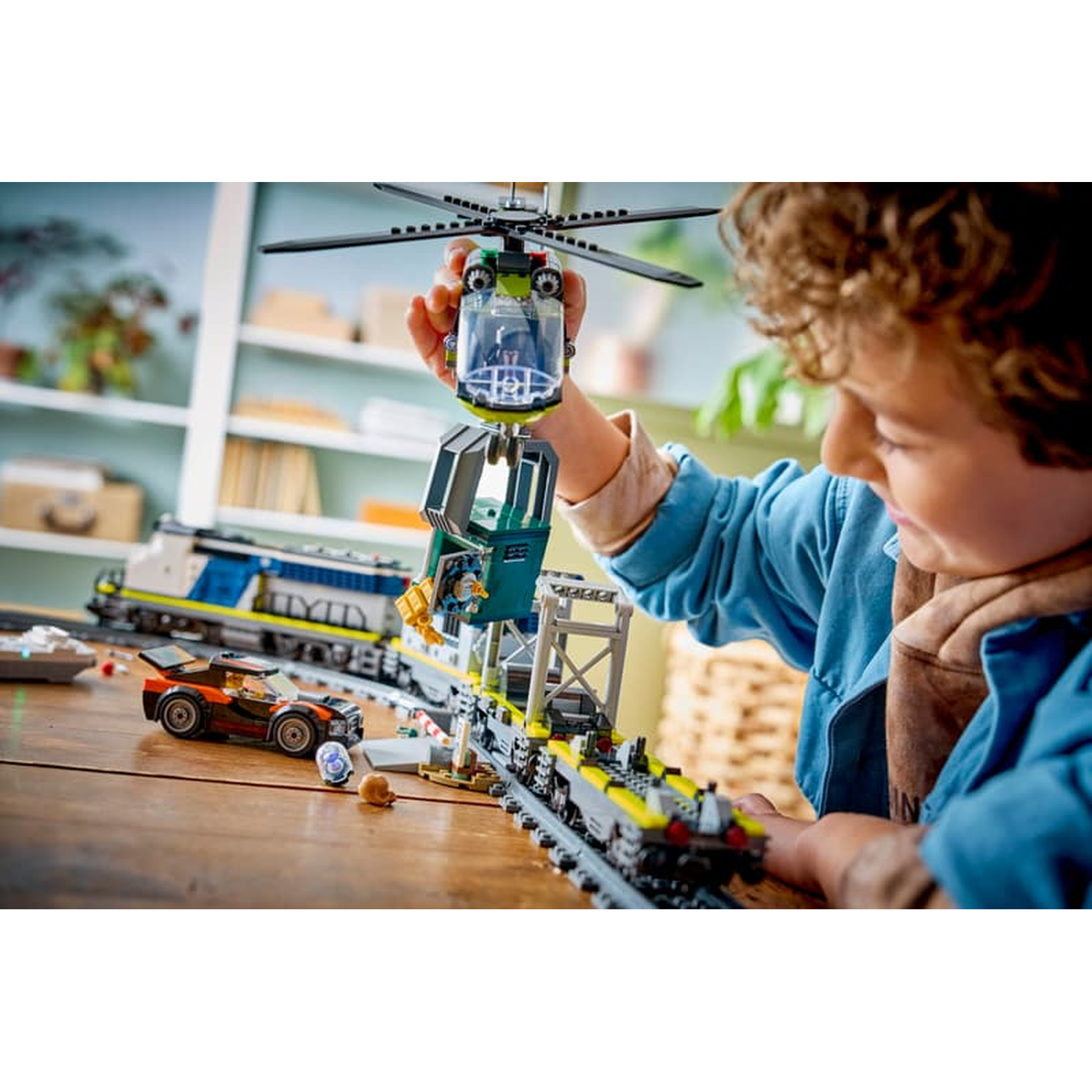 Child plays with Lego train, helicopter lifts cargo car.