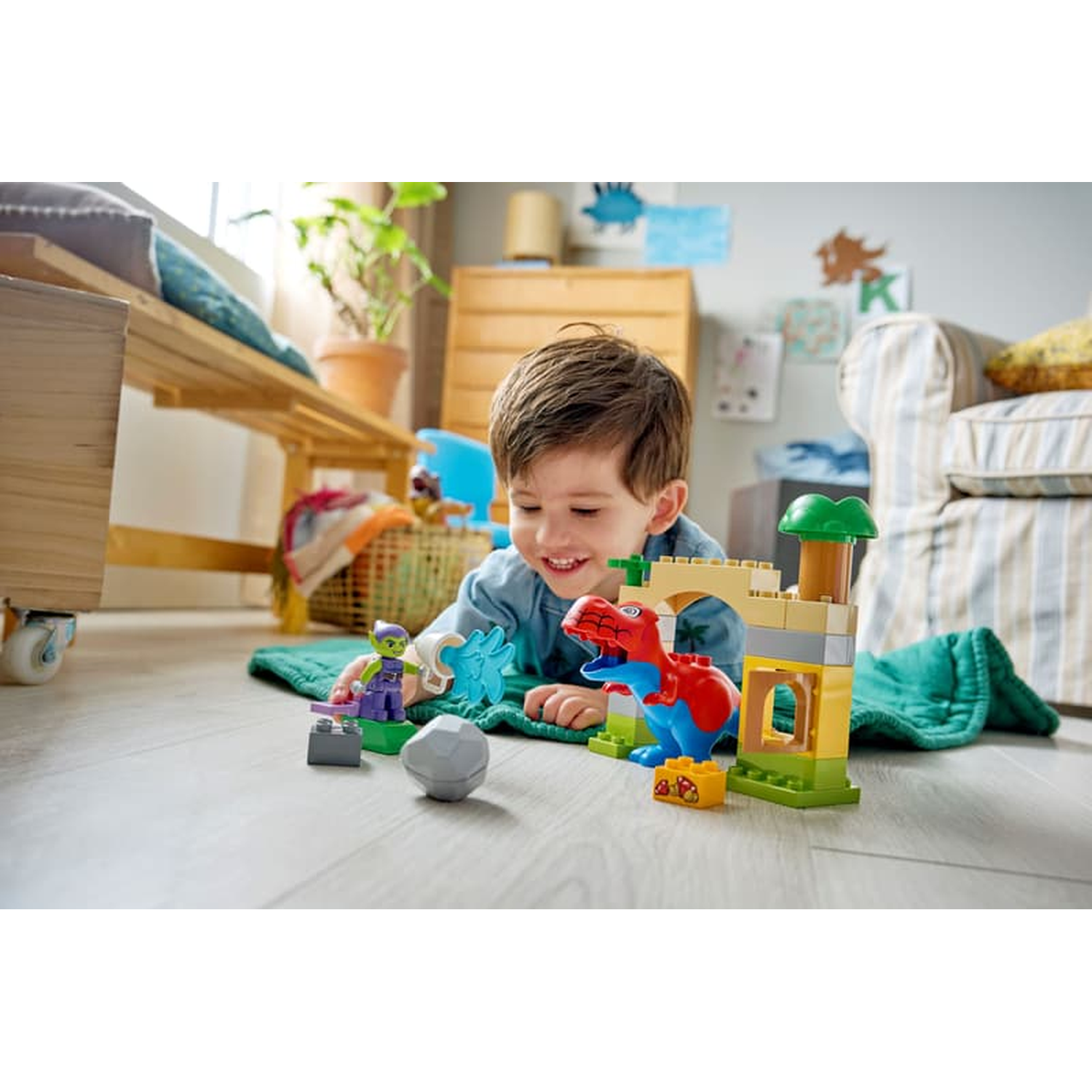 Un garçon joue avec des dinosaures et des figurines Lego par terre.