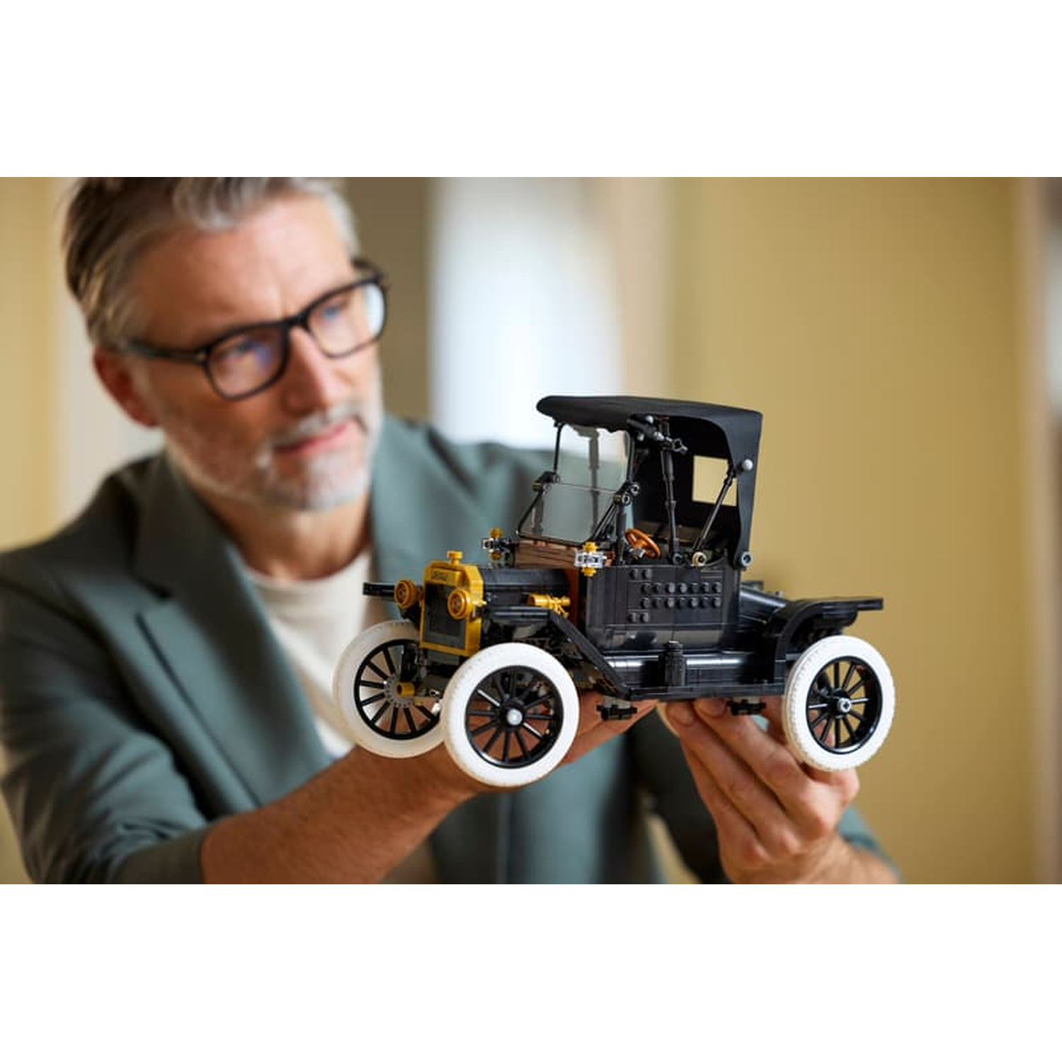 Een man houdt een gedetailleerde zwarte modelauto met witte velgen vast.