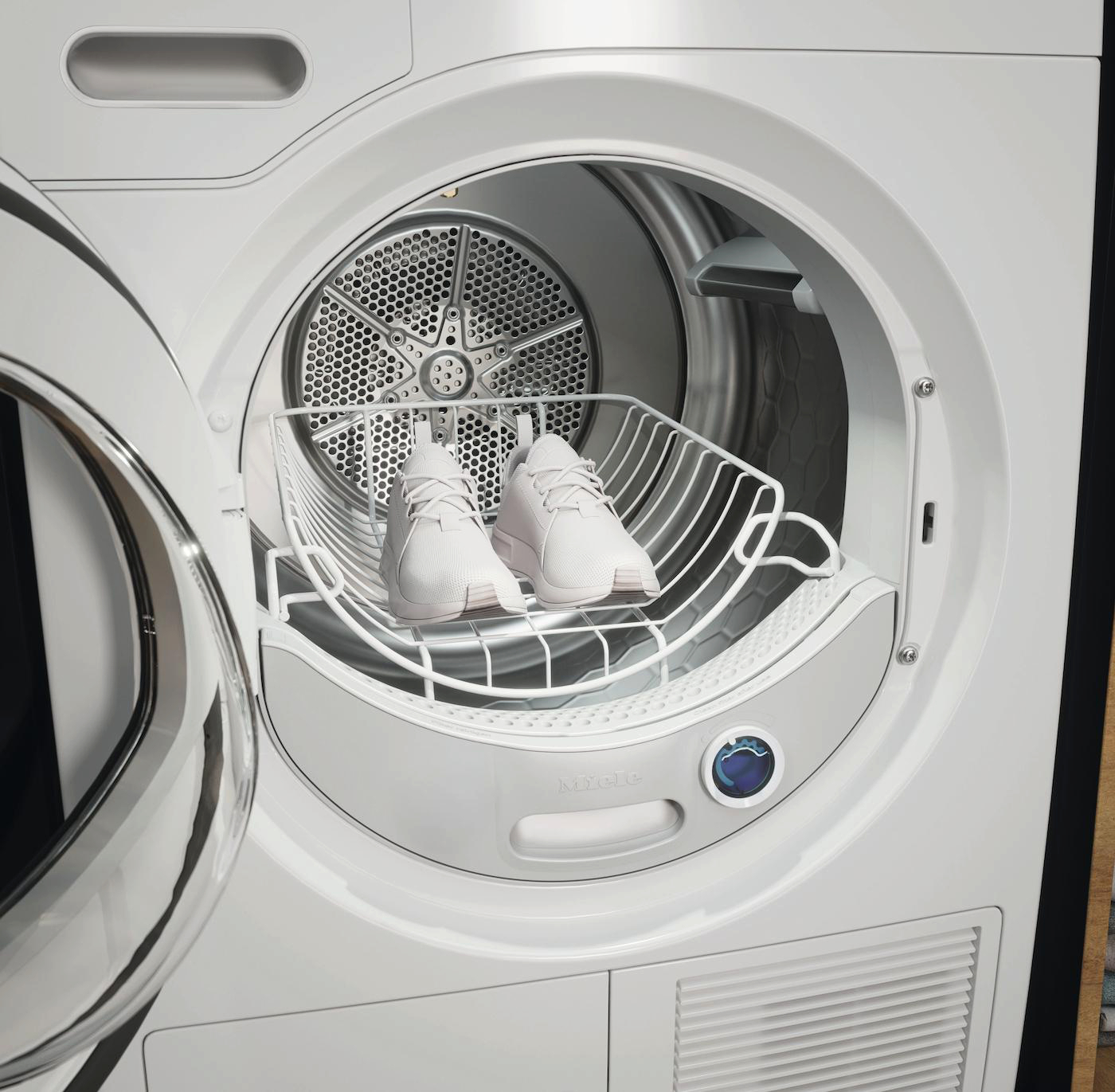 Weiße Turnschuhe in einem Wäschetrockner auf einem Schuhkorb.