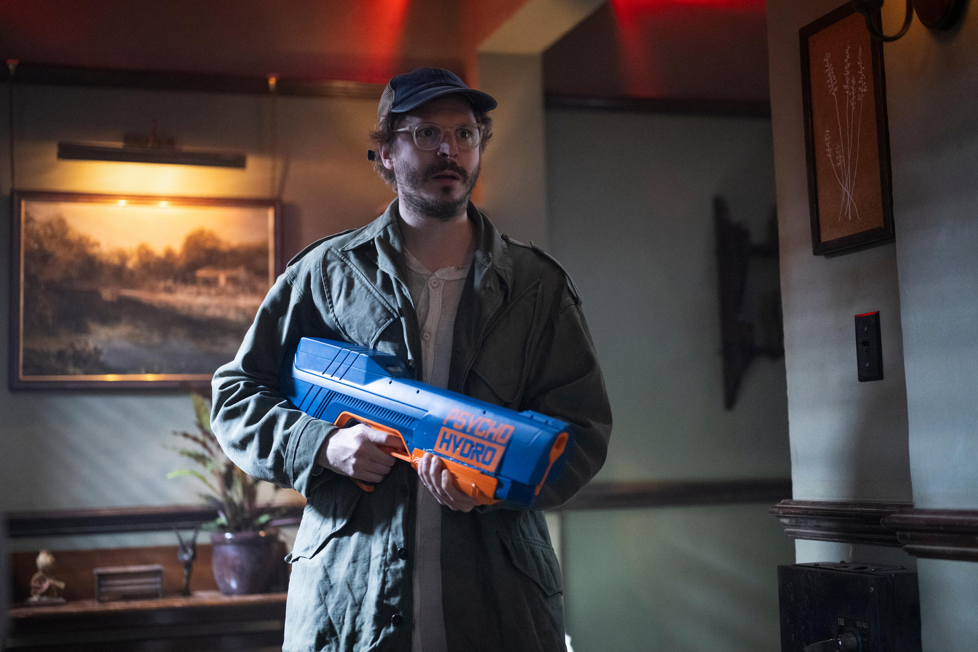 Ein Mann mit Brille und Kappe hält eine blaue und orangefarbene Wasserpistole.