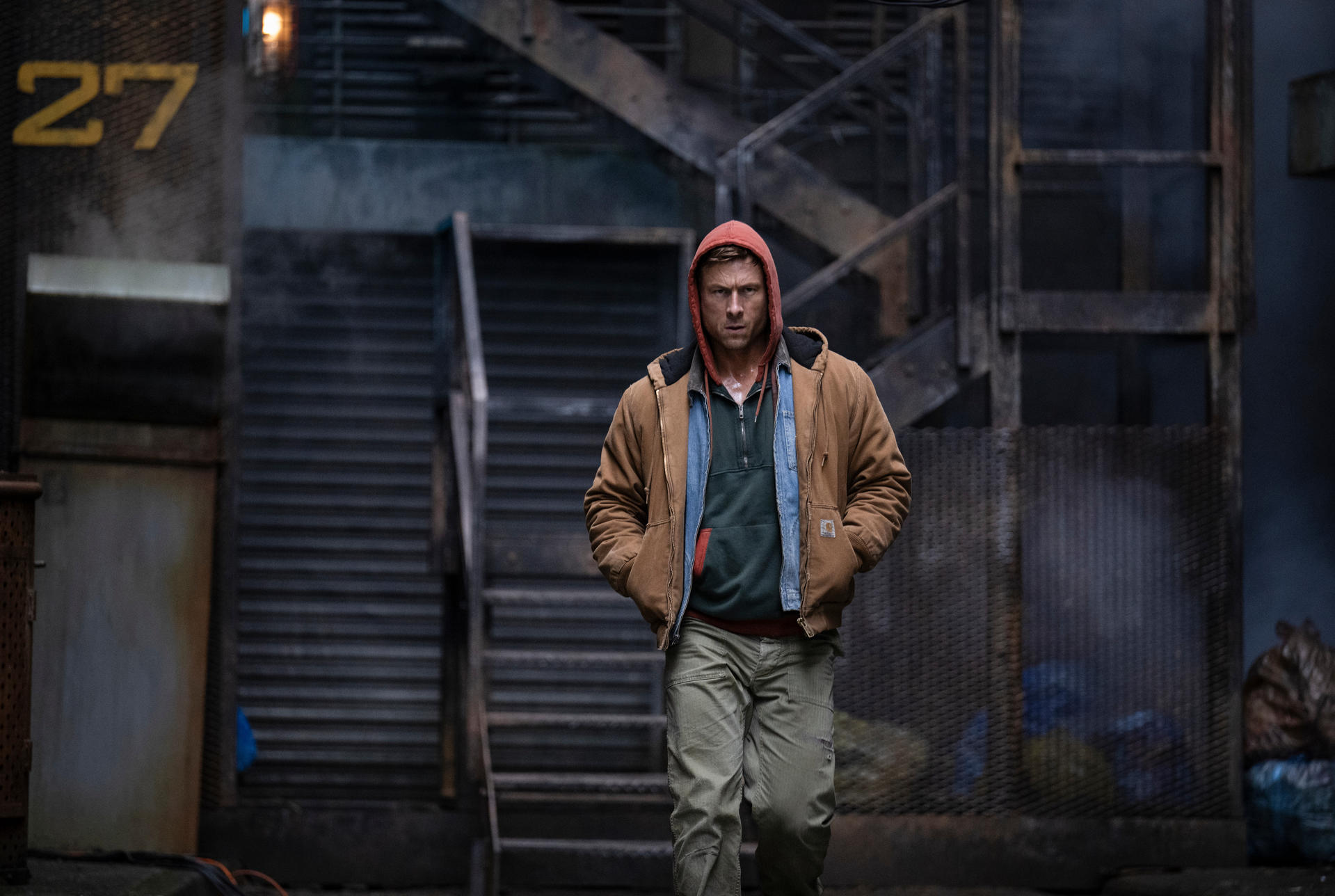 Mann in Kapuzenpullover und brauner Jacke geht auf Treppe zu.