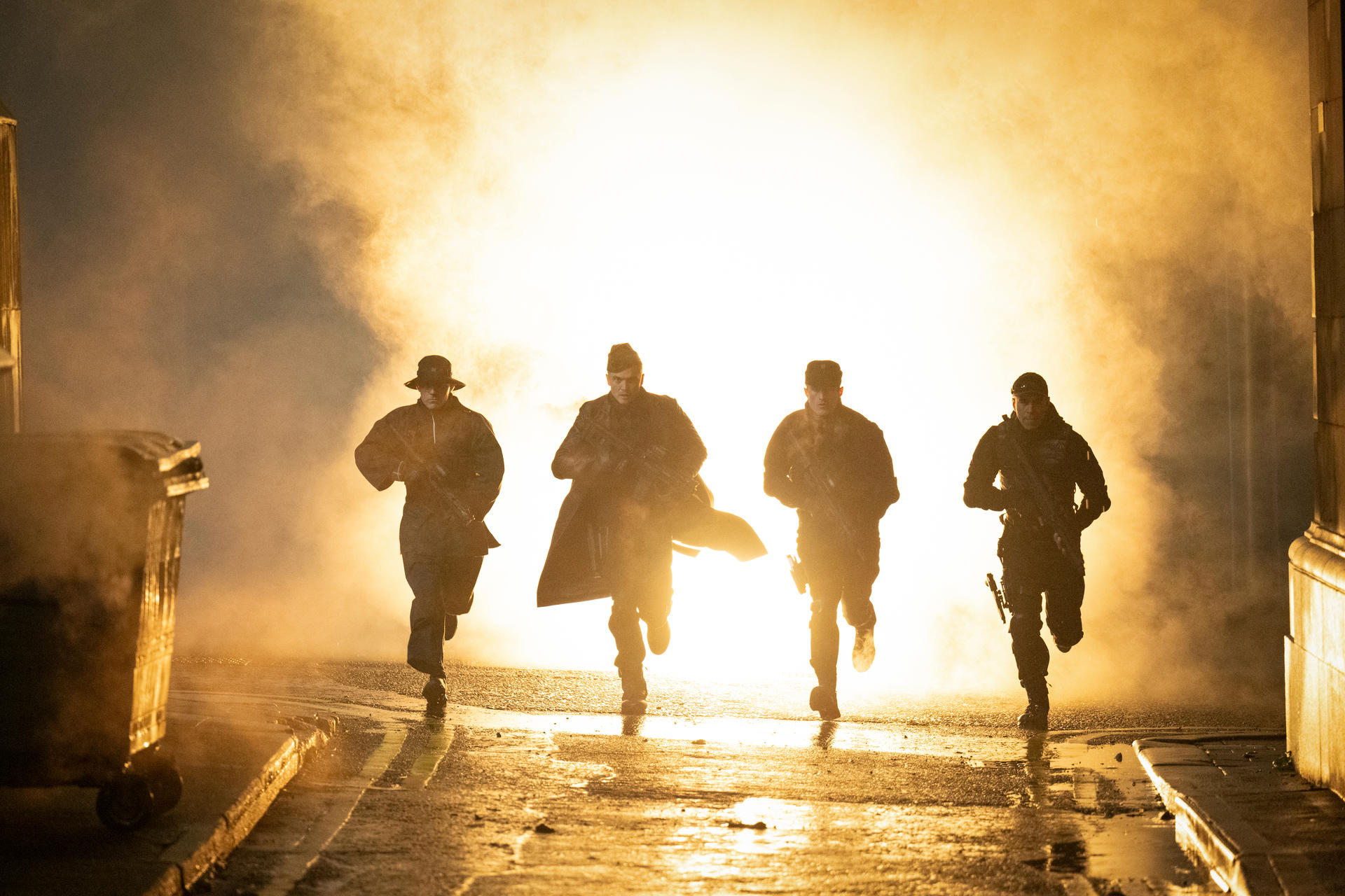 Vier Soldaten rennen durch neblige, beleuchtete Straße bei Nacht.