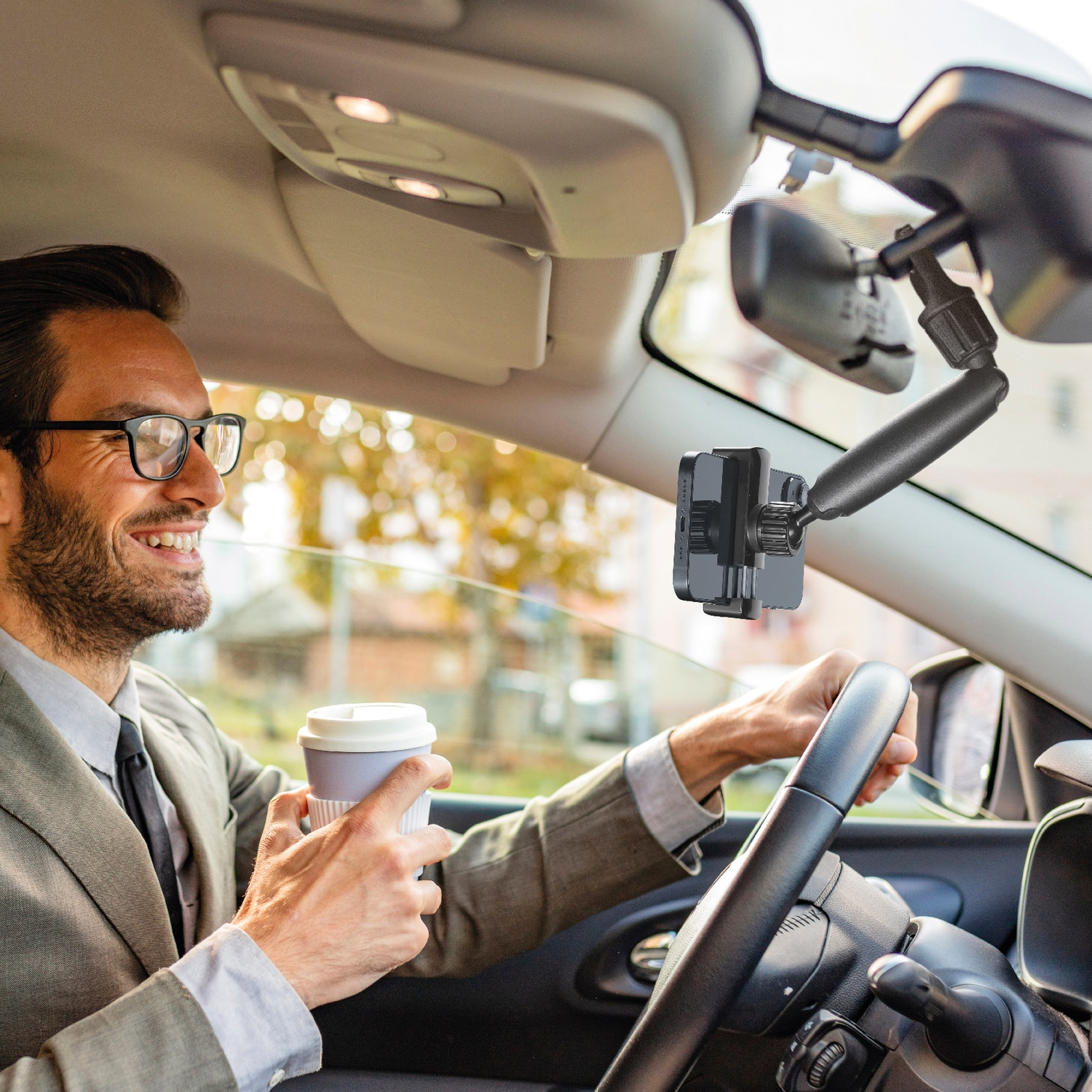 Un uomo in abito guida un'auto tenendo una tazza di caffè. È installato un supporto per telefono.