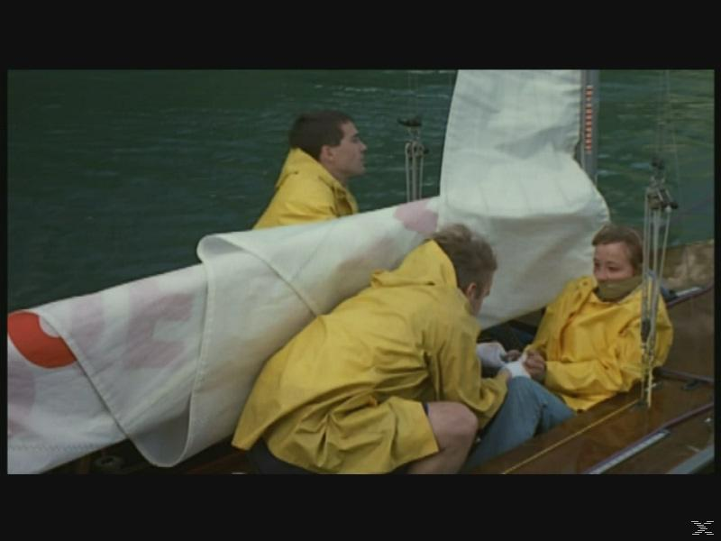 Drei Personen in gelben Regenjacken auf einem Segelboot mit weißen Segeln.