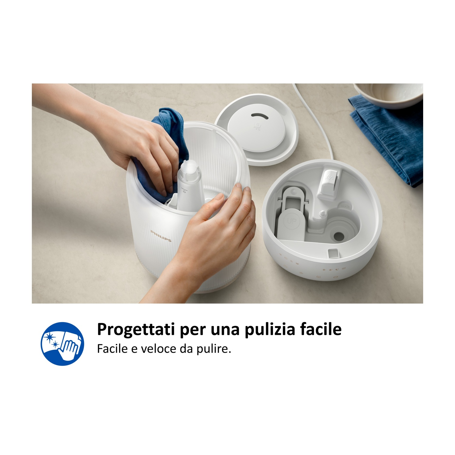 Parti bianche di umidificatore Philips su un piano di lavoro. Mani puliscono il dispositivo con un panno blu.