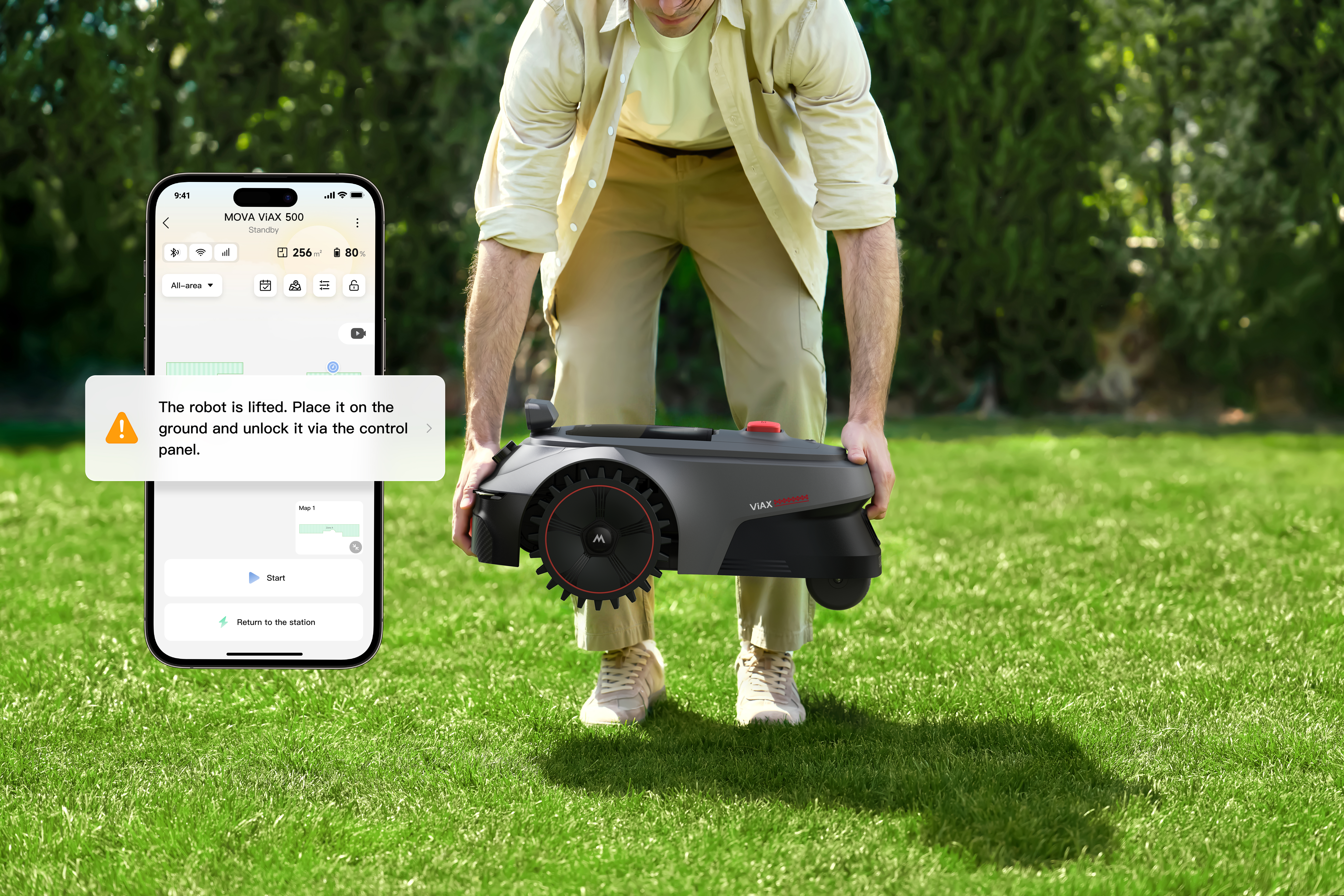 Mann hält einen grauen Mähroboter. Eine Handy-App zeigt eine Warnung.