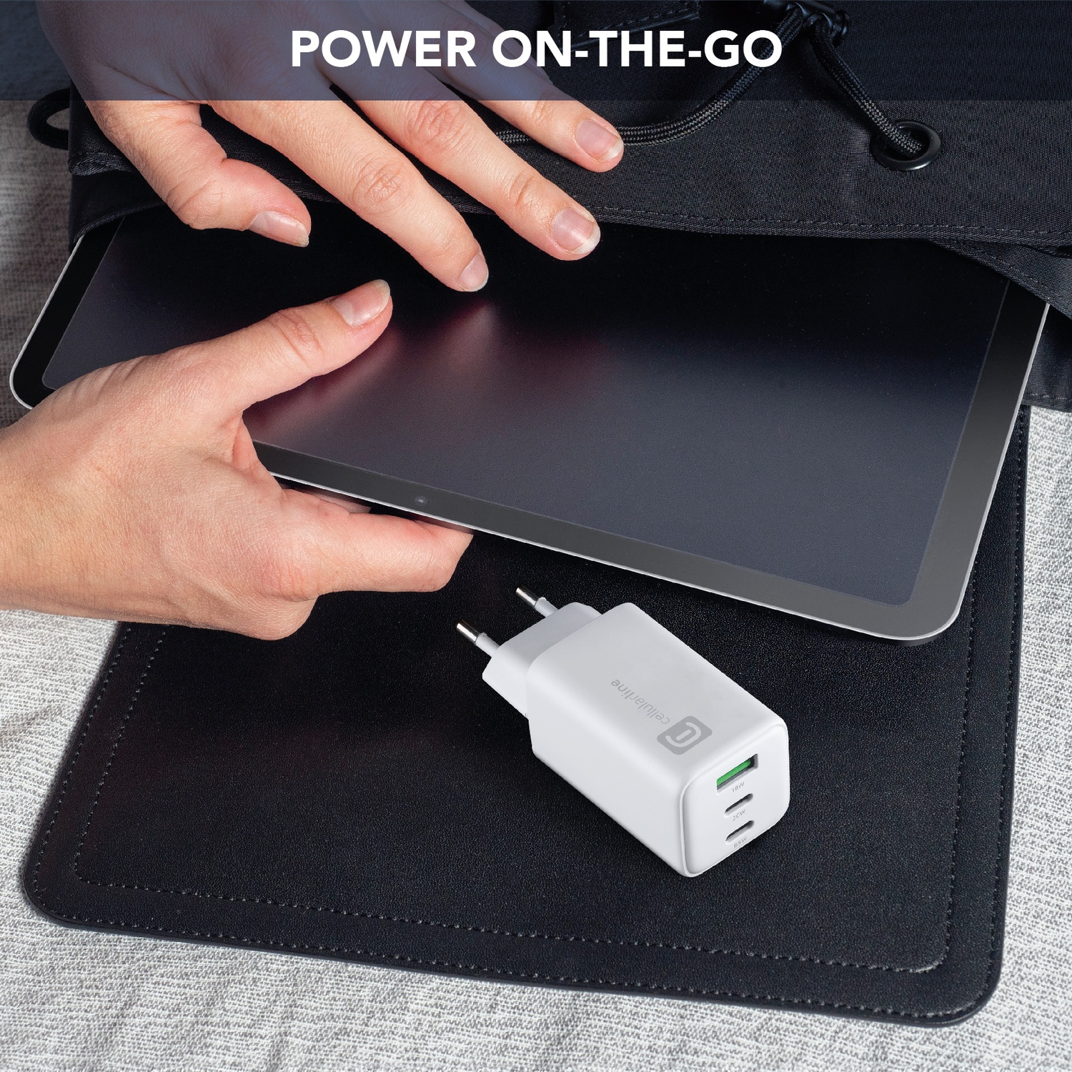 Un caricabatterie bianco con due porte USB poggia su un tappetino nero accanto a un tablet.