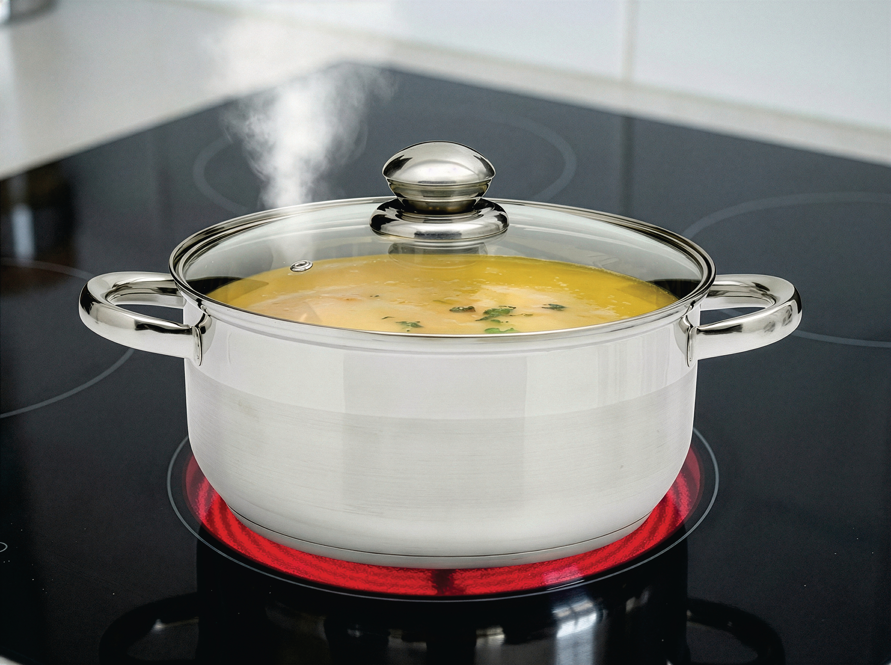 Ein Topf mit gelber Suppe kocht auf einem Kochfeld. Dampf steigt auf.