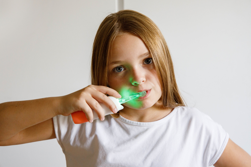 Dziewczynka myje zęby świecącą szczoteczką.