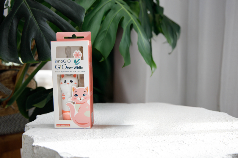 Opakowanie szczoteczki do zębów dla dzieci z motywem kota, obok rośliny.