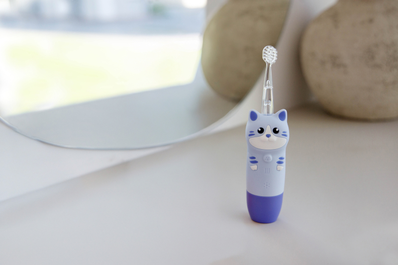 Jasnoniebieska szczoteczka do zębów w kształcie kota z fioletowymi akcentami stoi na białej powierzchni.