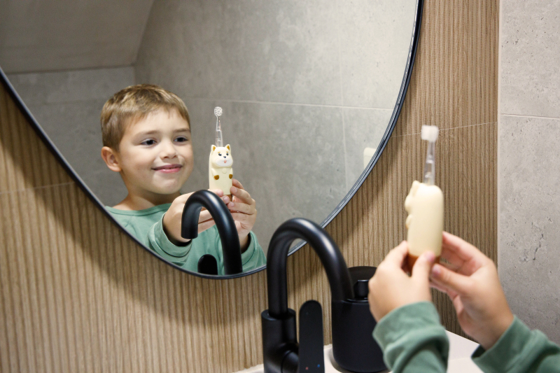 Chłopiec w lustrze trzyma szczoteczkę do zębów ze zwierzątkiem.