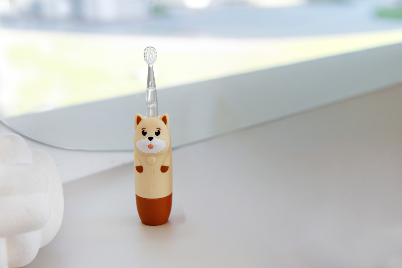 Beżowo-biała szczoteczka do zębów dla dzieci w kształcie psa stoi na powierzchni.