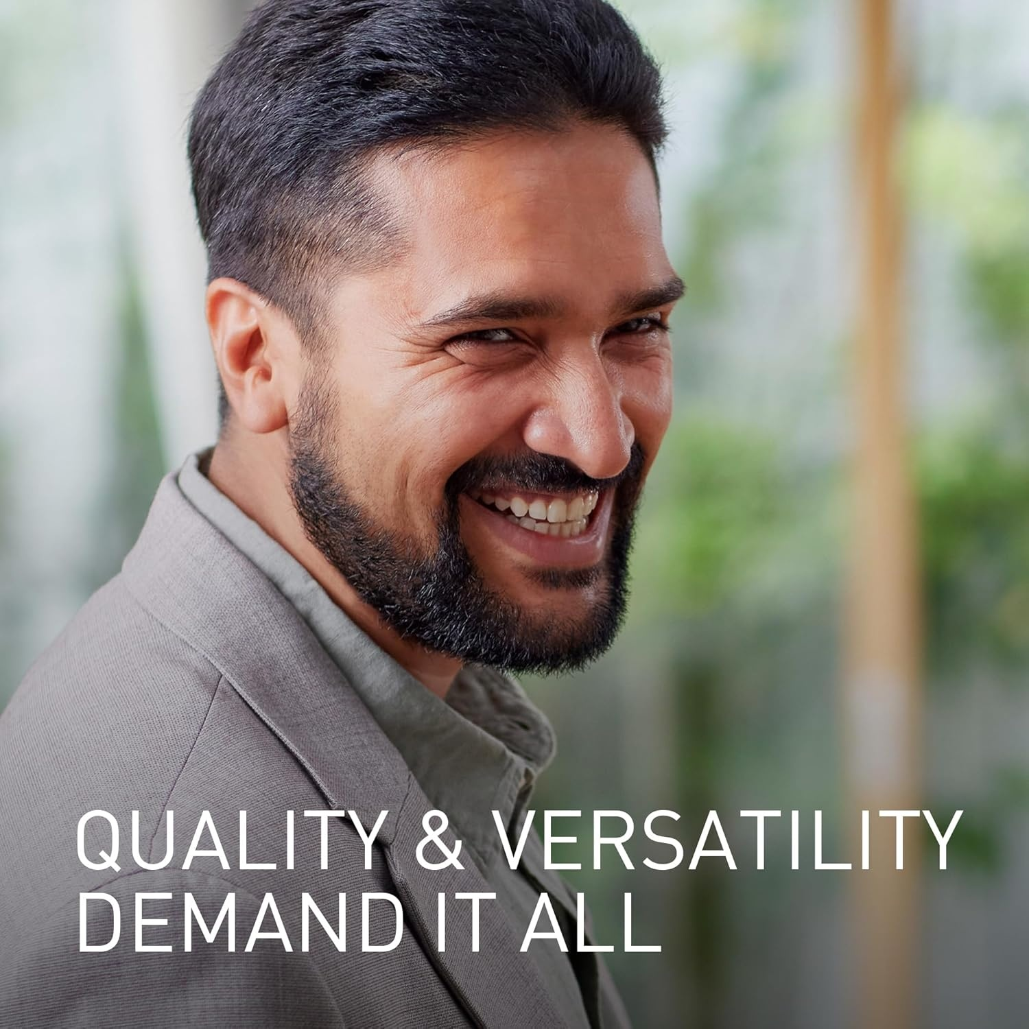Un uomo con barba sorride in completo grigio. Testo: QUALITY & VERSATILITY DEMAND IT ALL.