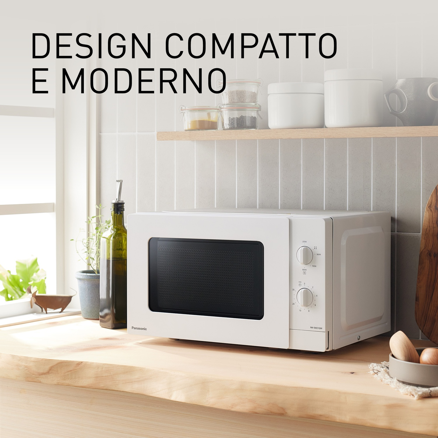 Un microonde bianco Panasonic su un bancone di legno con bottiglie nelle vicinanze.