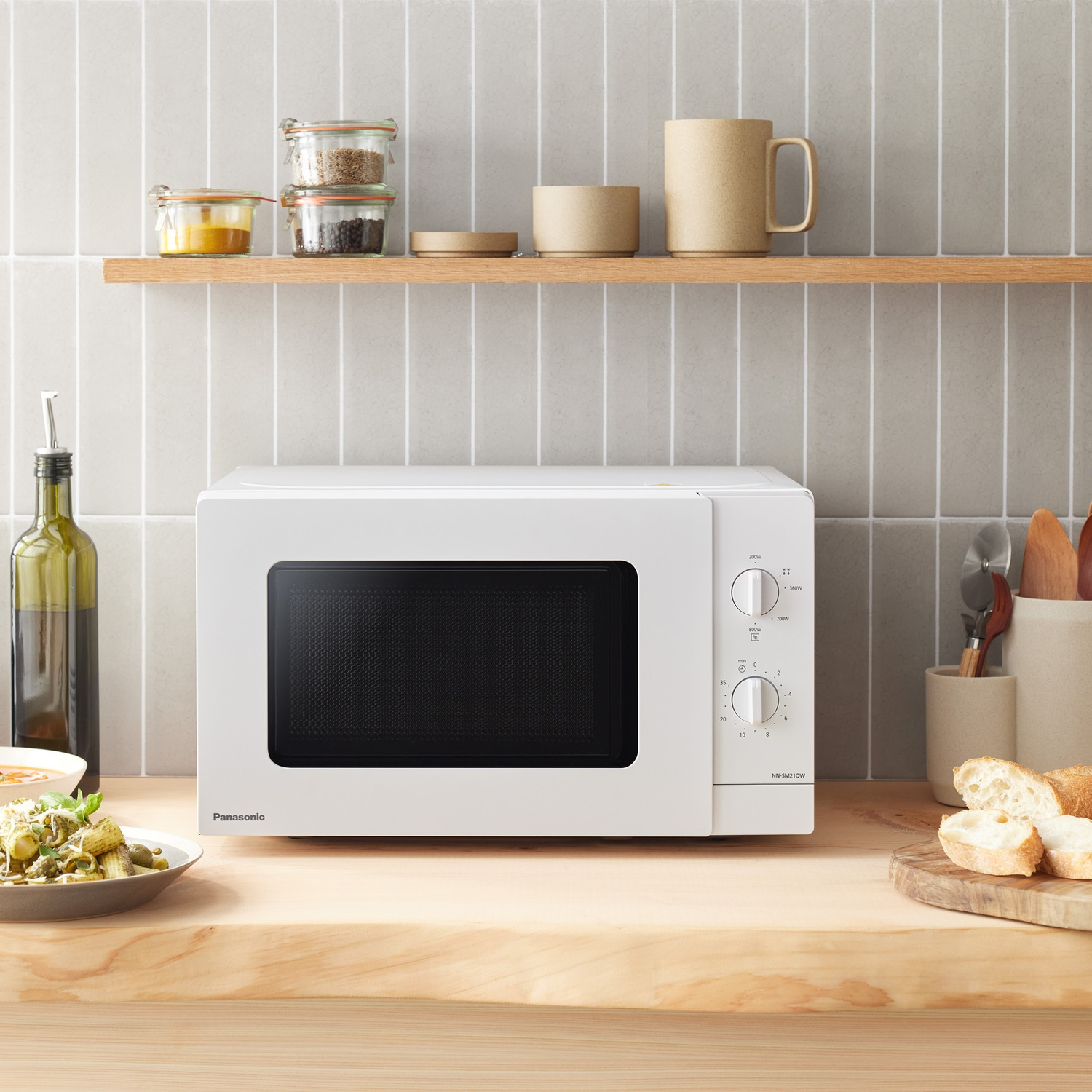 Un microonde Panasonic bianco è su un bancone di legno. A sinistra c'è un piatto di pasta.