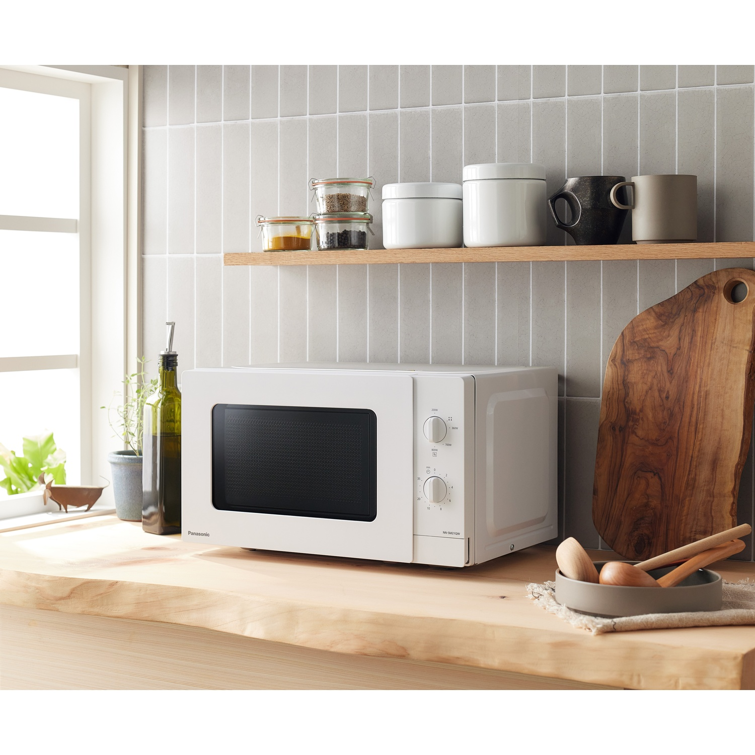 Un microonde bianco su un bancone di legno con utensili da cucina.