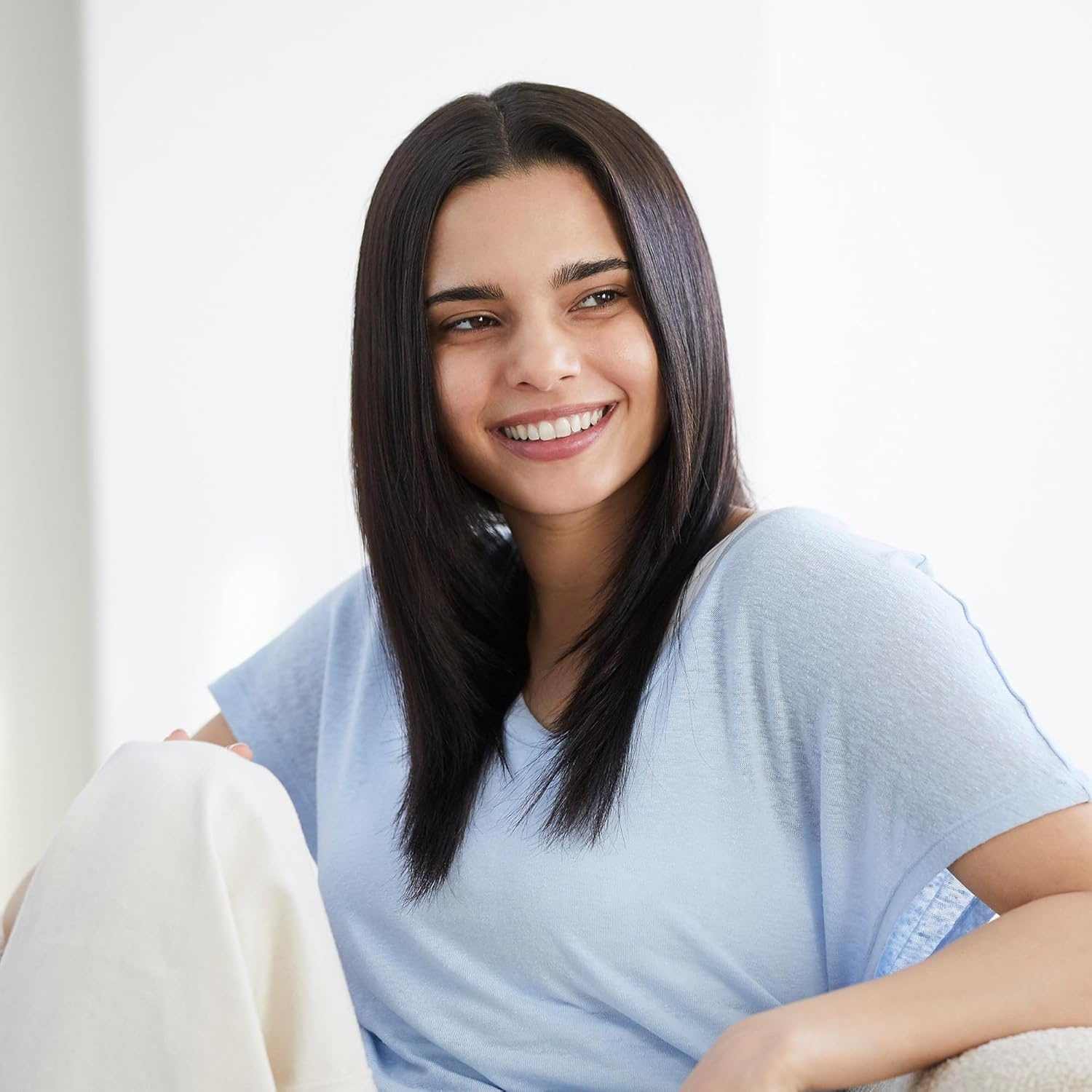 Una giovane donna con capelli scuri sorride, indossa un top azzurro.