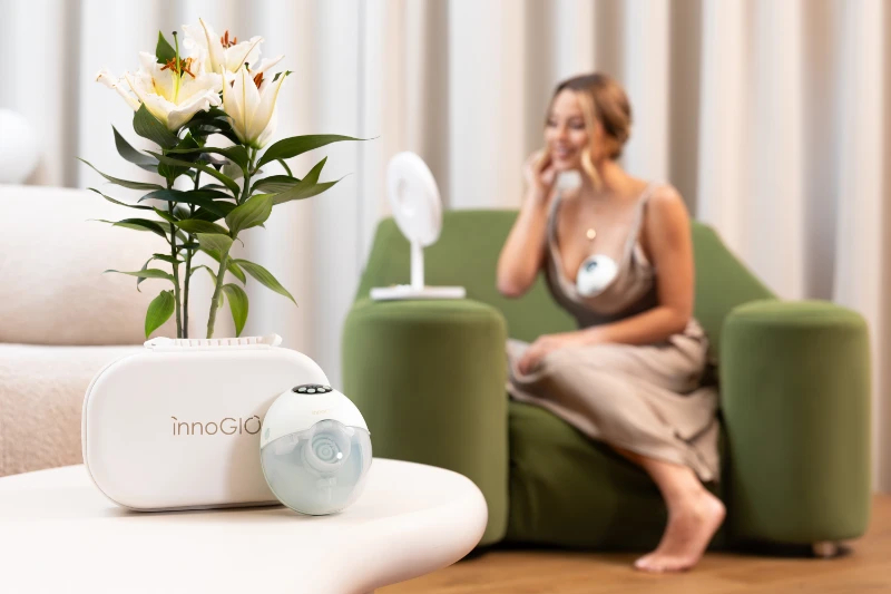 Białe lilie obok laktatora i etui. Kobieta siedzi na sofie.