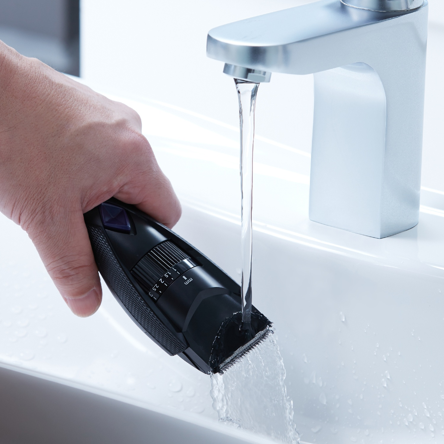 Una mano sciacqua un tagliacapelli nero sotto l'acqua corrente in un lavandino.