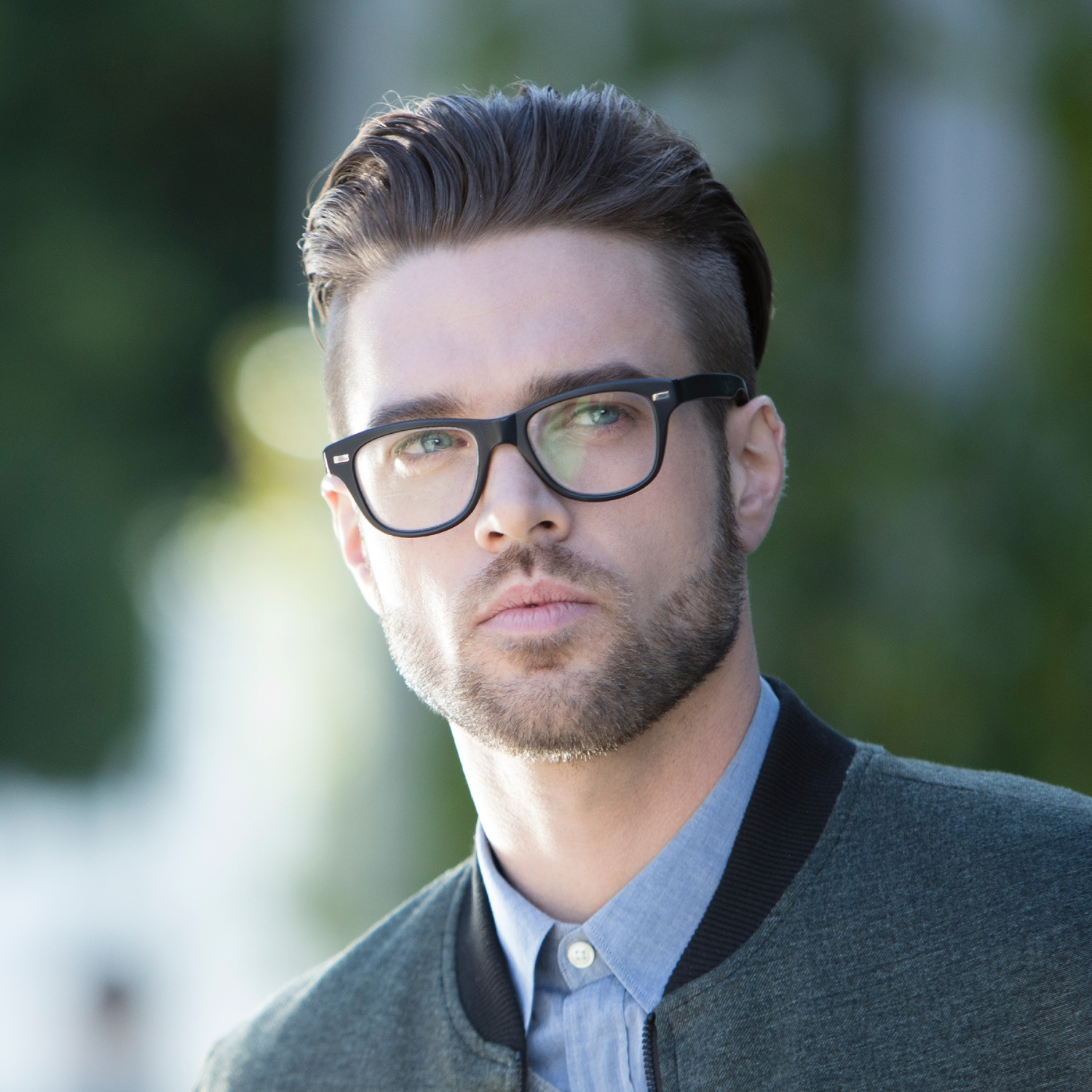 Un uomo con occhiali e barba, giacca grigia su camicia blu.