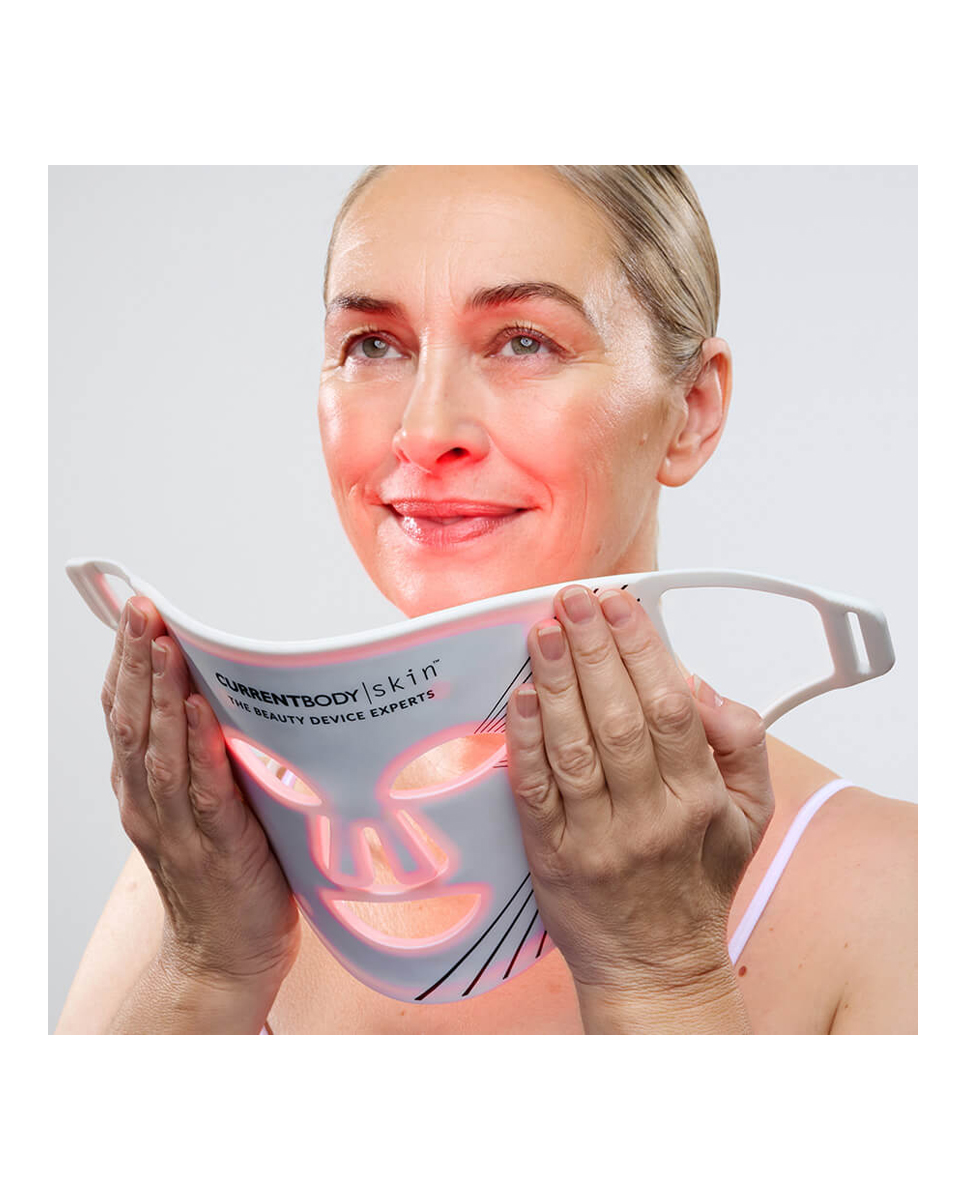 Mujer sosteniendo una mascarilla facial LED blanca con luz roja.