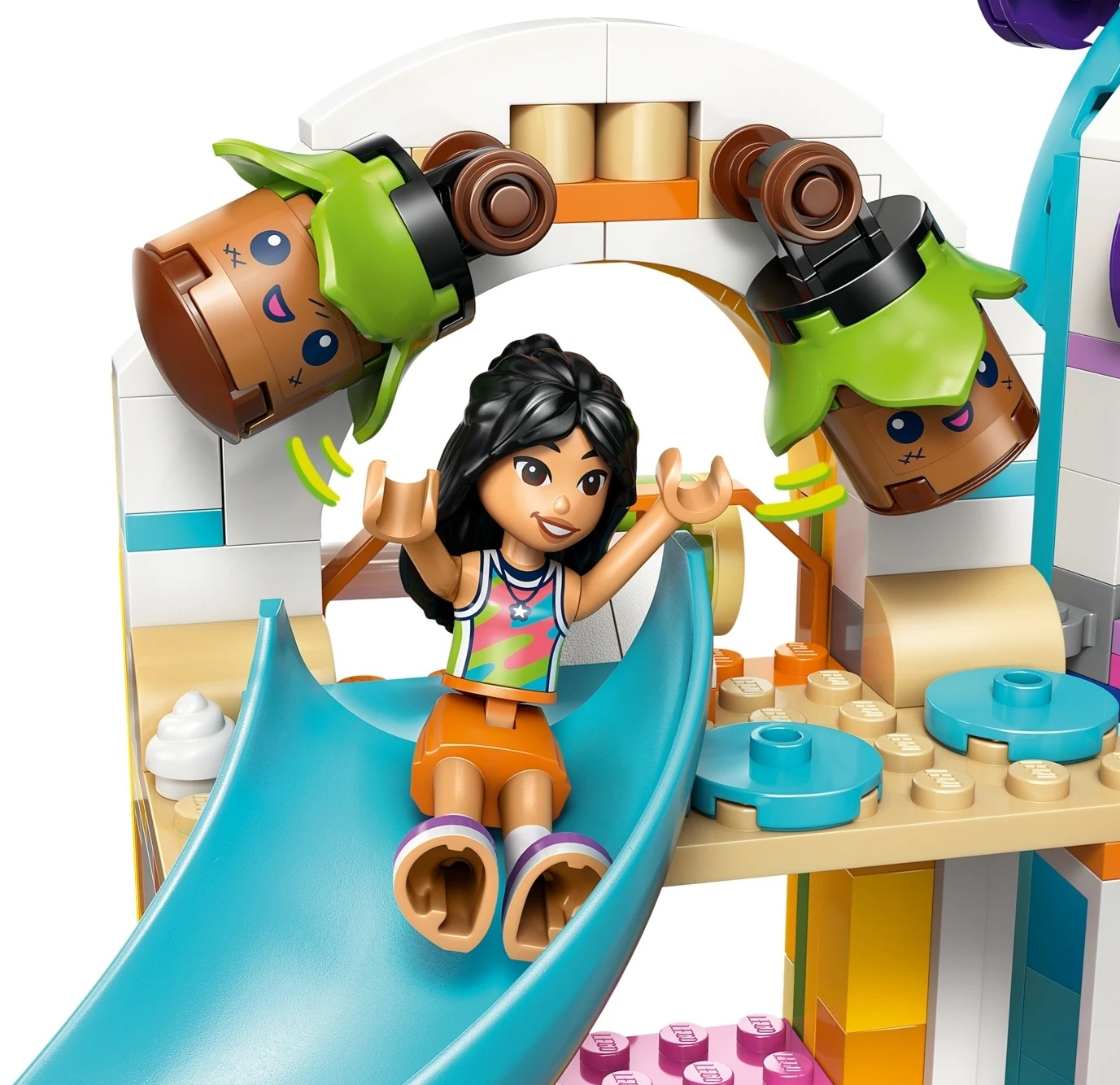 Dziewczynka Lego zjeżdża po niebieskiej zjeżdżalni, uśmiechnięte doniczki wiszą powyżej.