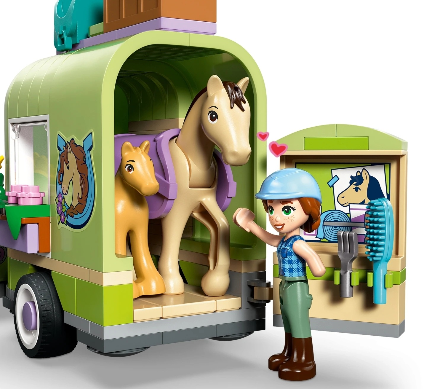 Dziewczynka z przyczepą dla koni z dwoma końmi w środku. Narzędzia i szczotka wiszą na ścianie.