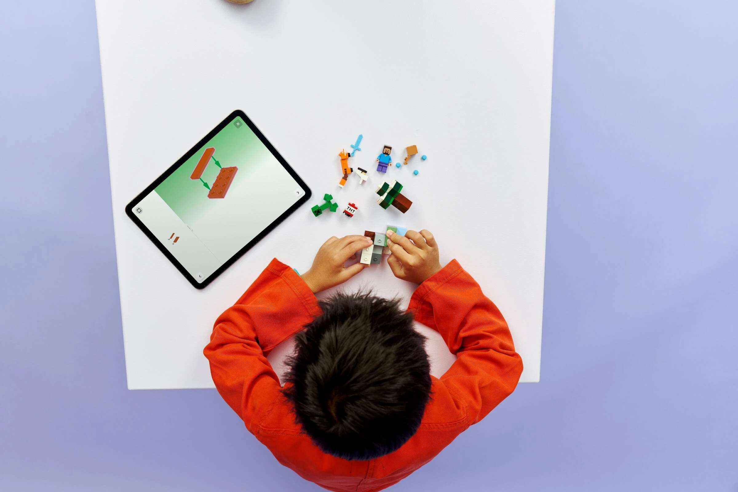 Dziecko bawi się figurkami Lego, budując obiekt, patrząc na tablet.