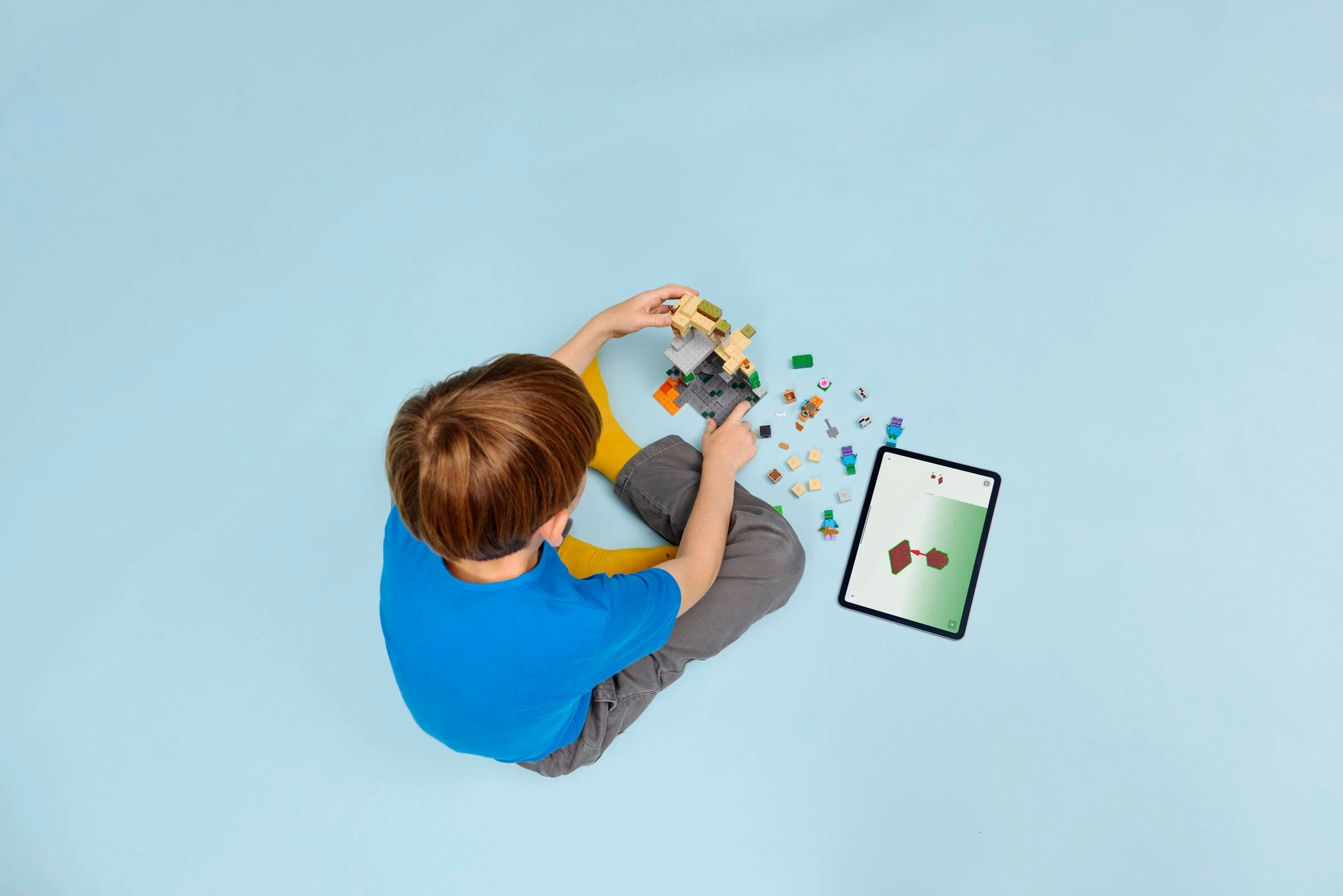 Chłopiec buduje z kolorowych klocków i patrzy na tablet z instrukcjami.