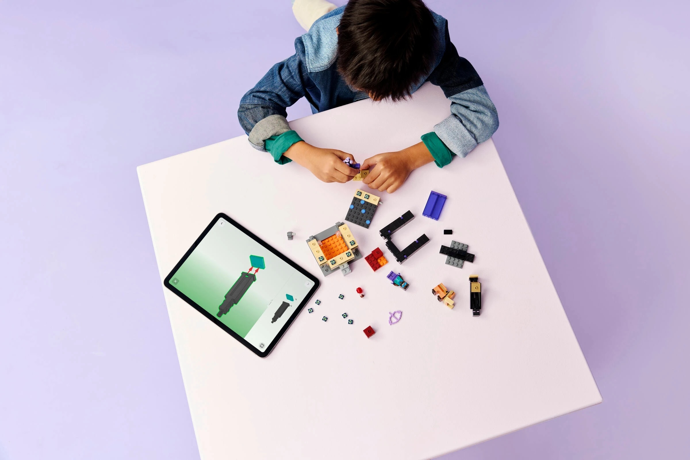 Chłopiec buduje z kolorowych klocków Lego, instrukcje są widoczne na tablecie.