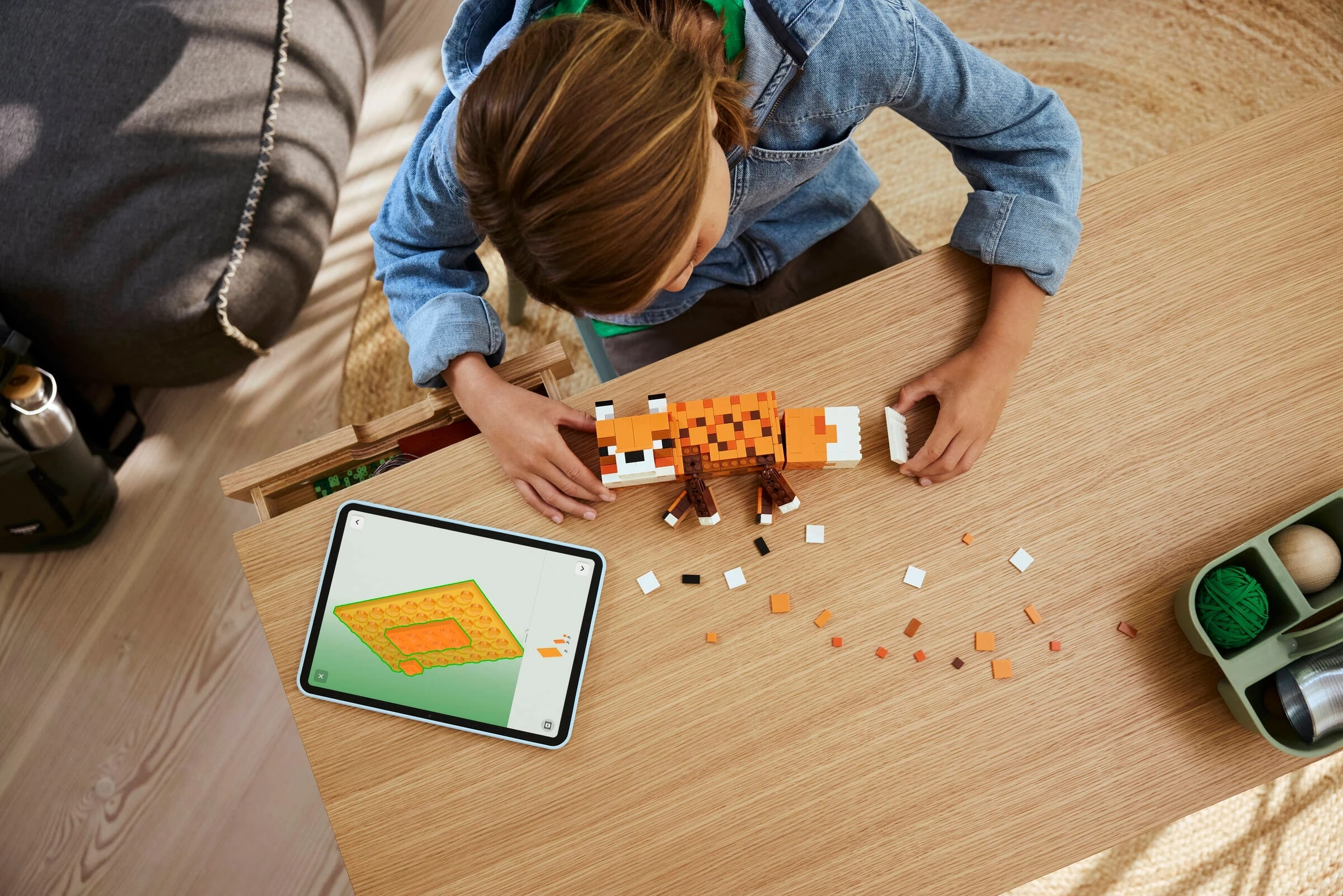 Dziecko buduje figurkę lisa z Lego, tablet pokazuje instrukcje. Rozrzucone pomarańczowe, białe, brązowe.