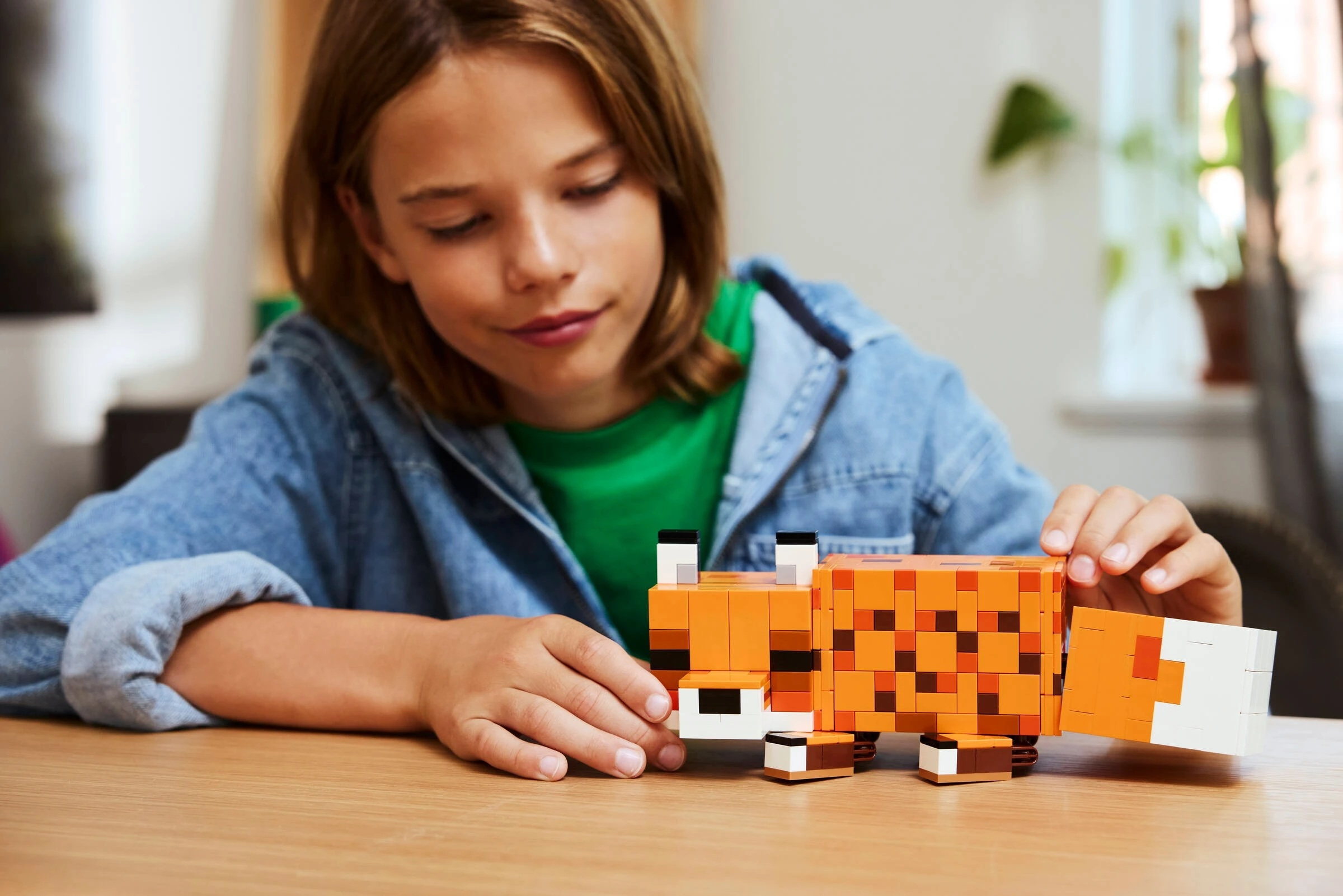 Chłopiec buduje pomarańczowego lisa z klocków Lego na drewnianym stole.