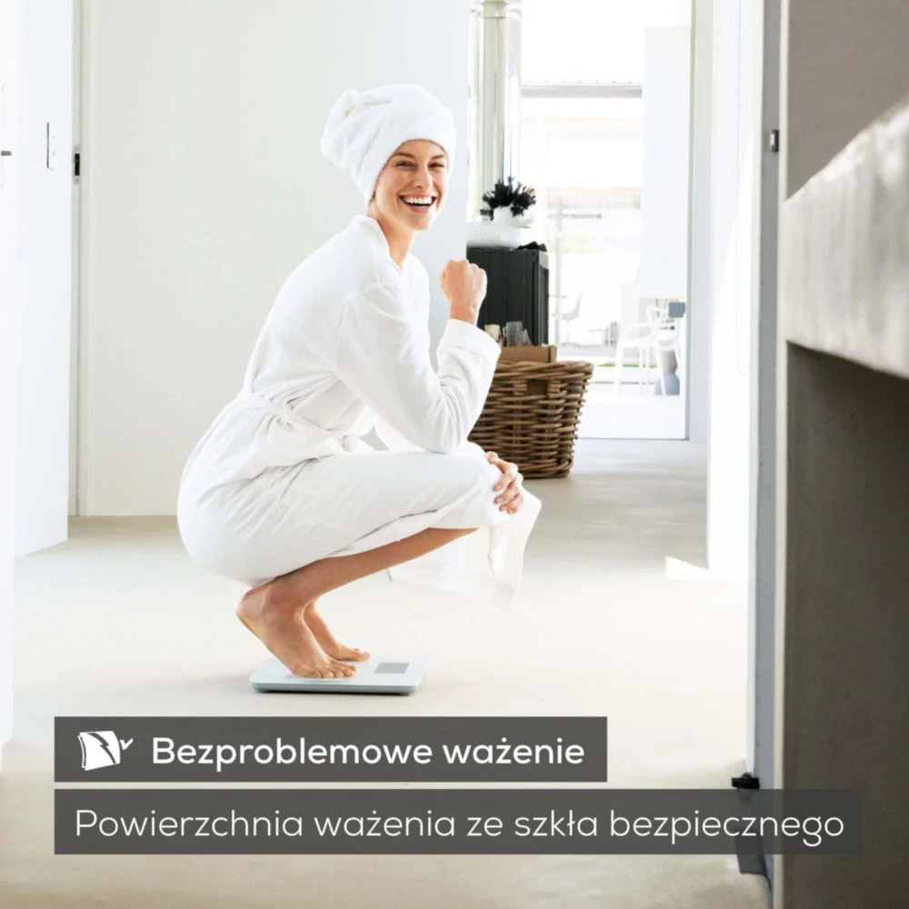 Kobieta w białym szlafroku i ręczniku kuca na wadze.