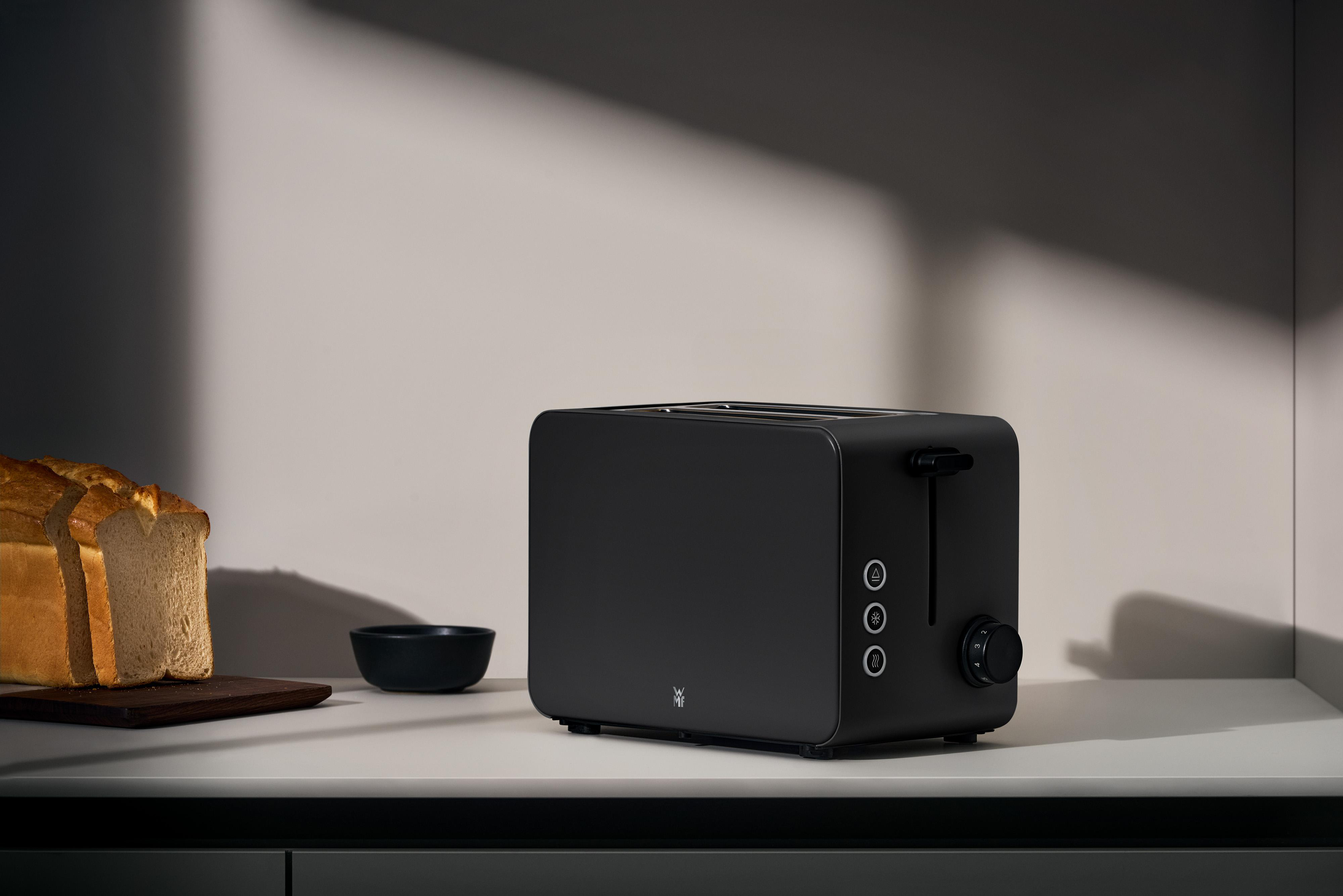 Ein schwarzer Toaster steht auf einer Arbeitsplatte neben Toastbrotscheiben und einer Schale.
