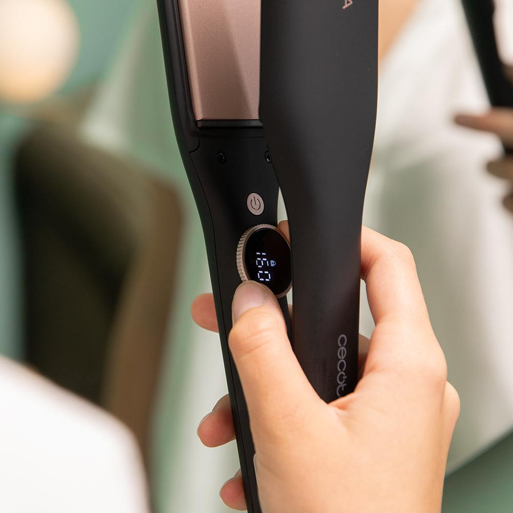Una mano sostiene una plancha de pelo negra con pantalla digital de temperatura de 160.